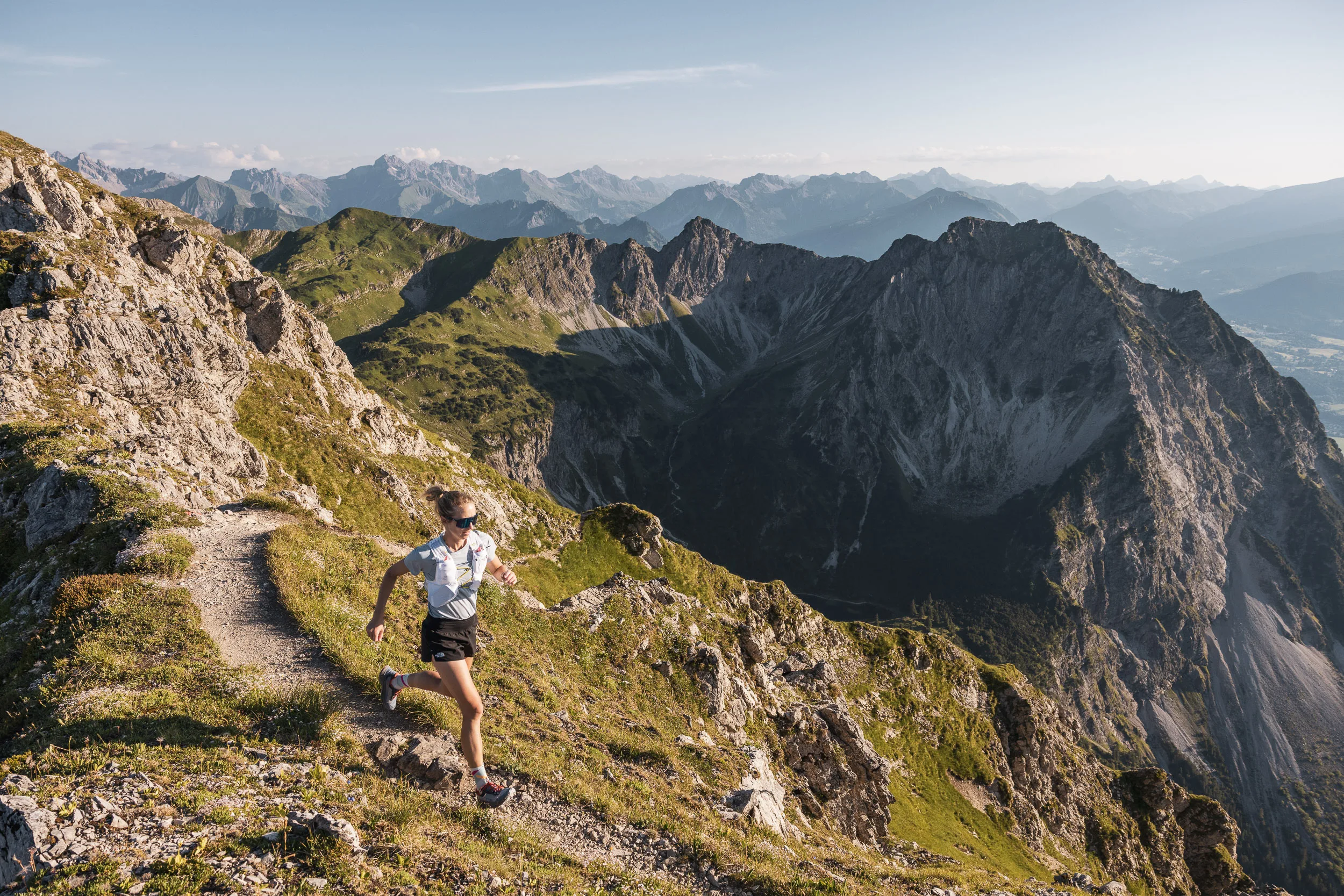 Trailrunnerin auf felsigem Pfad vor weitem Bergpanorama