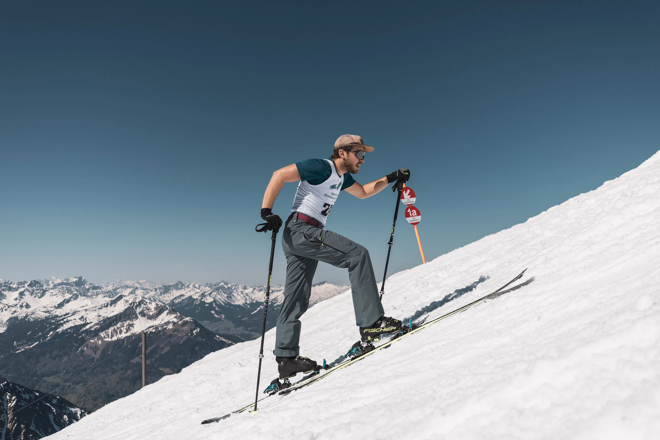 Skitourenläufer im dynamischen Aufstieg gegen den blauen Himmel, unten das Bergpanorama des Allgäus