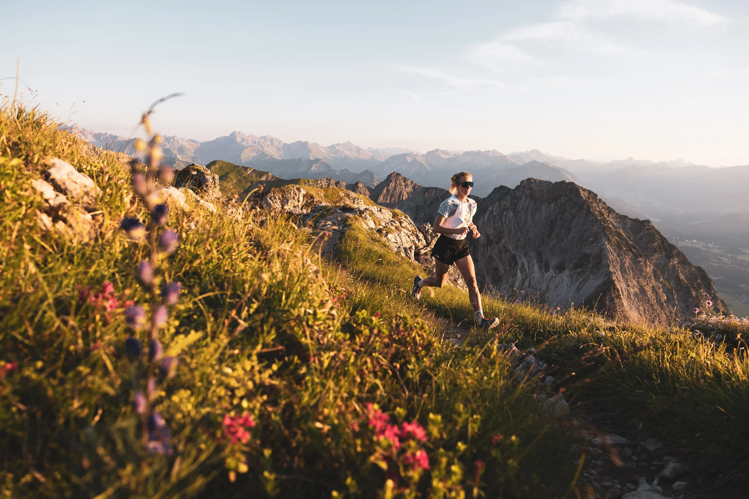 Trailrunnerin zwischen Bergblumen im warmen Licht des Sommerabends