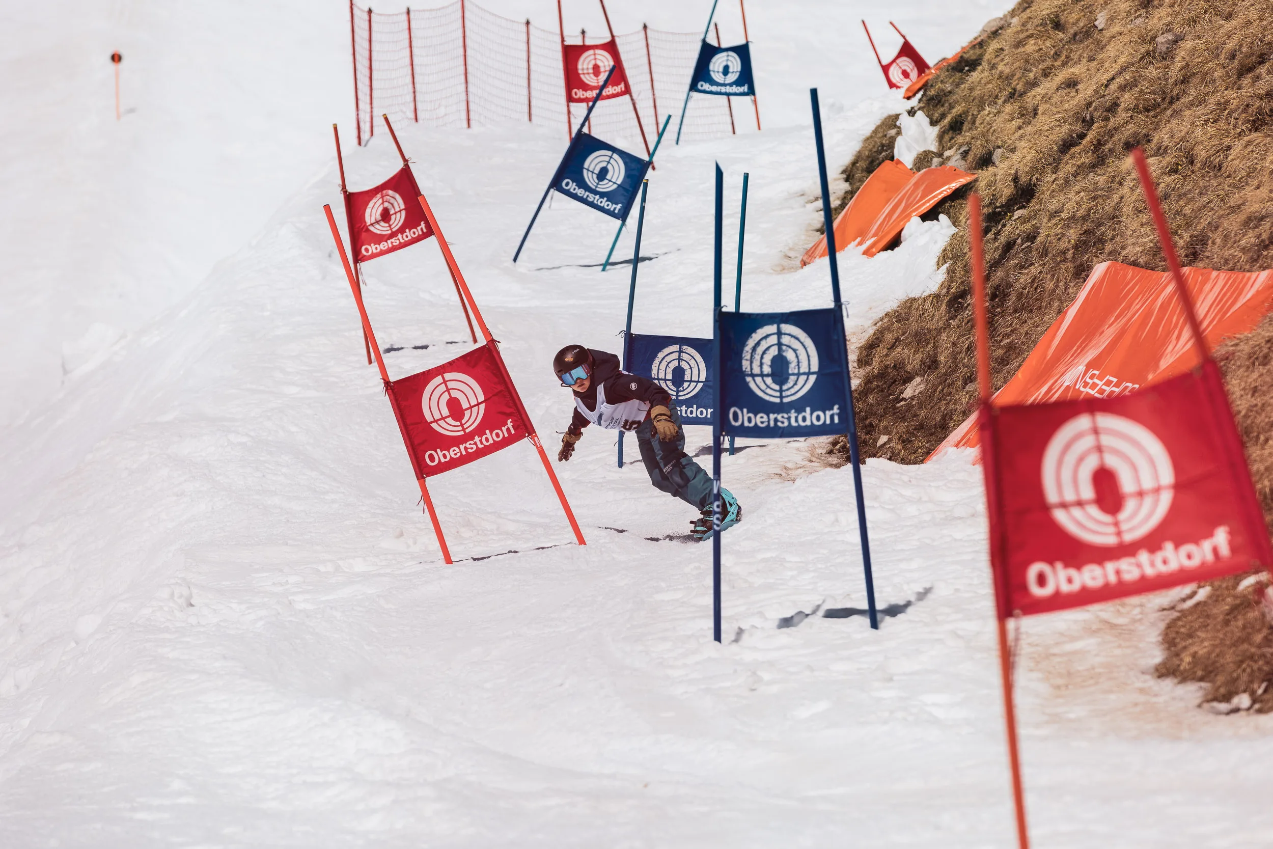 Snowboarder fährt durch die rot-blauen Oberstdorf-Tore des Banked Slalom über den Frühlingsfirn
