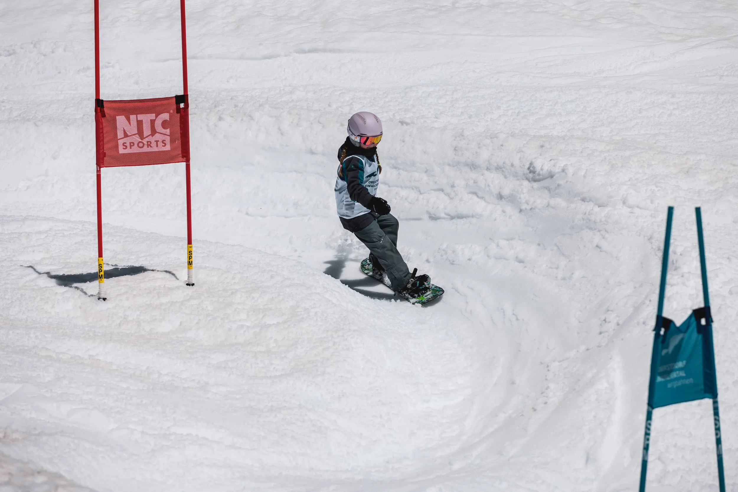 Kind auf dem Snowboard im Kids Banked Slalom fährt konzentriert durch ein rotes Tor