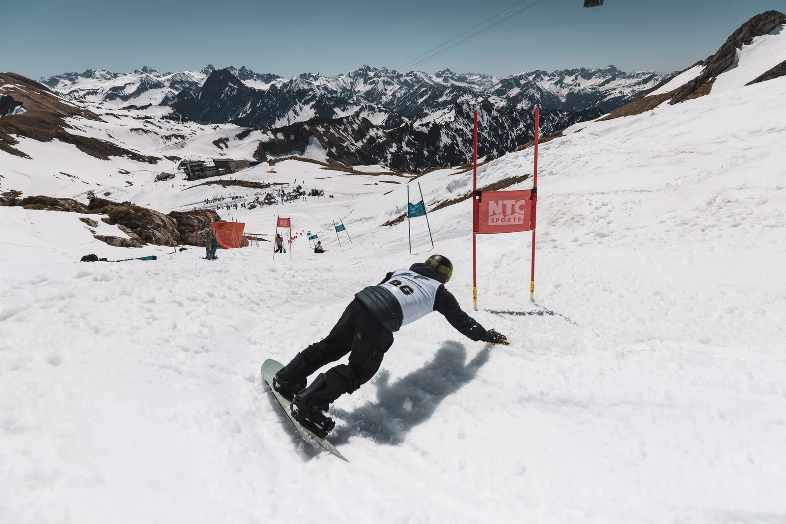 Snowboarder carvt im Banked Slalom über den Frühlingsfirn, dahinter das weite Allgäuer Bergpanorama