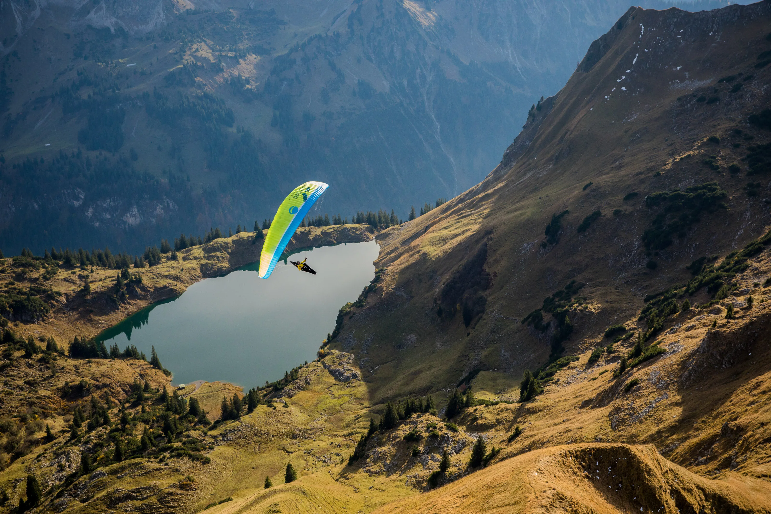 Michael Gebert unter grünem Gleitschirm über dem Seealpsee mit steilen herbstlichen Flanken am Nebelhorn