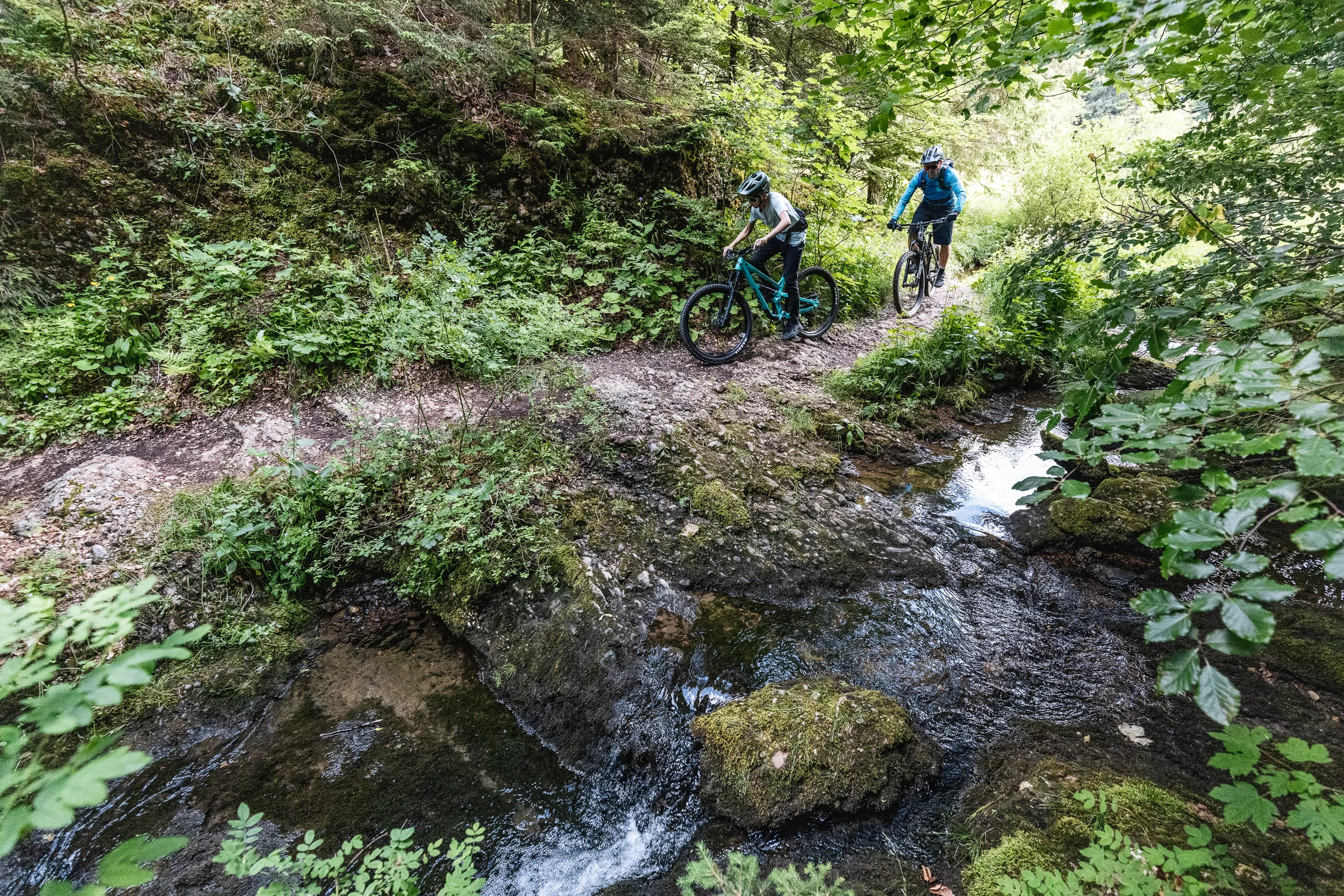 Florian Häusler und Kilian Morell fahren an einen schmalen Bachlauf im Bergwald