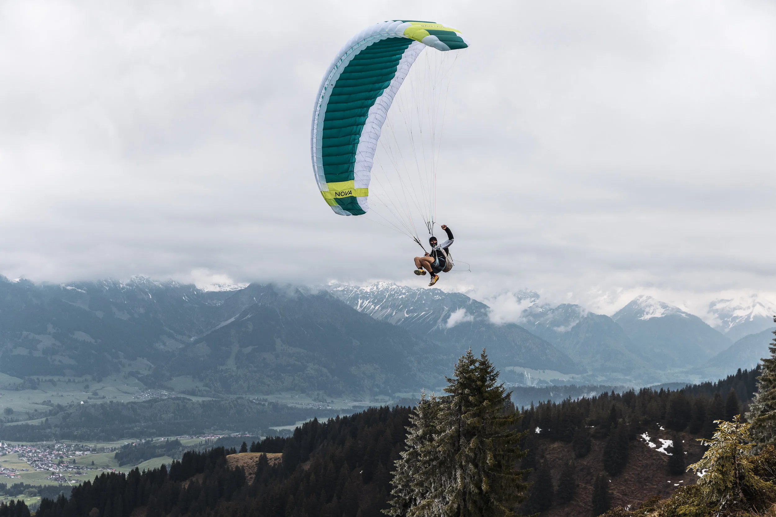 Gleitschirmpilot fliegt über bewaldeten Hängen und einem weiten Tal im Allgäu