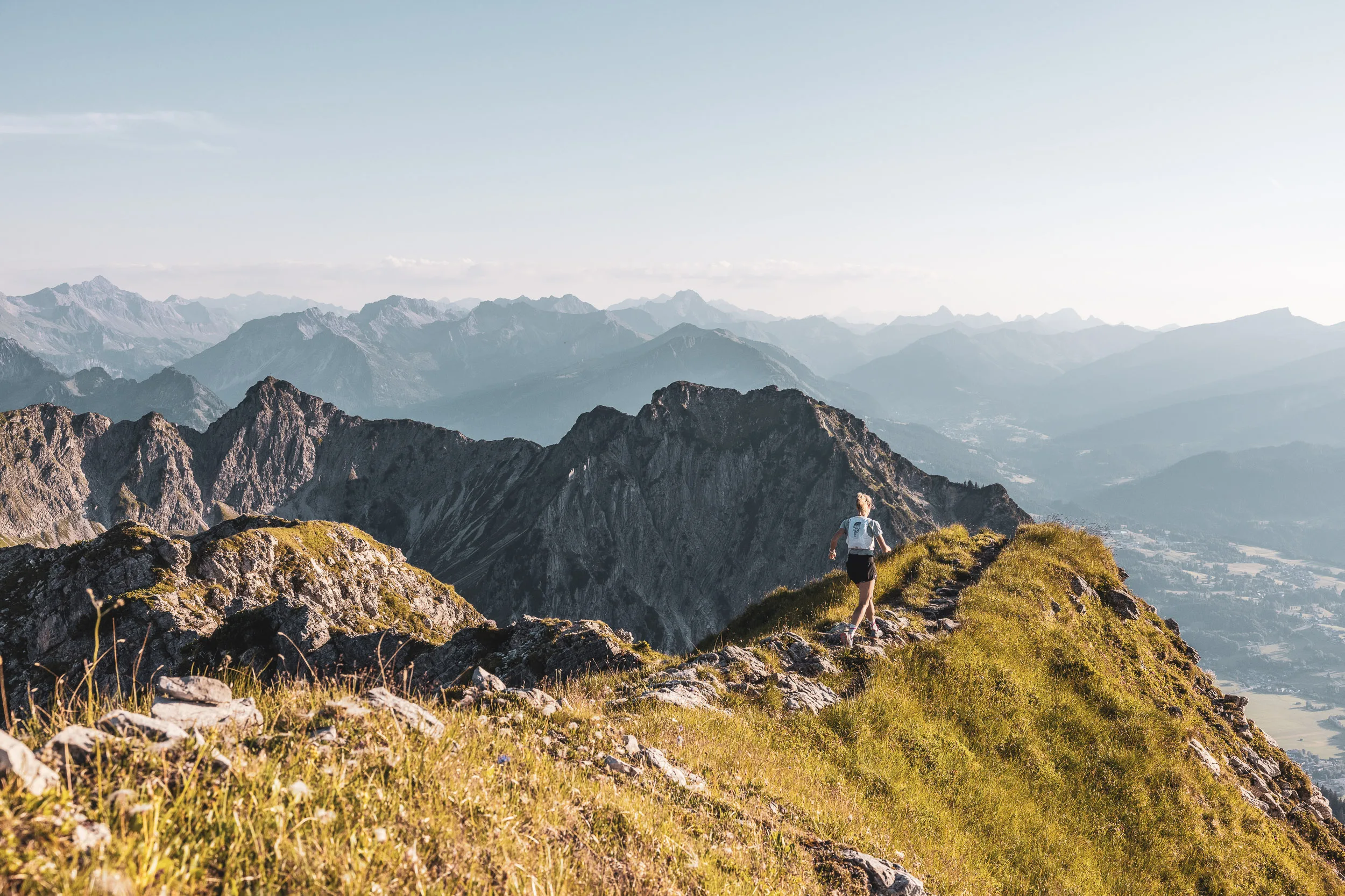 Trailrunnerin auf einem sonnigen Grat mit Blick über die Allgäuer Alpen