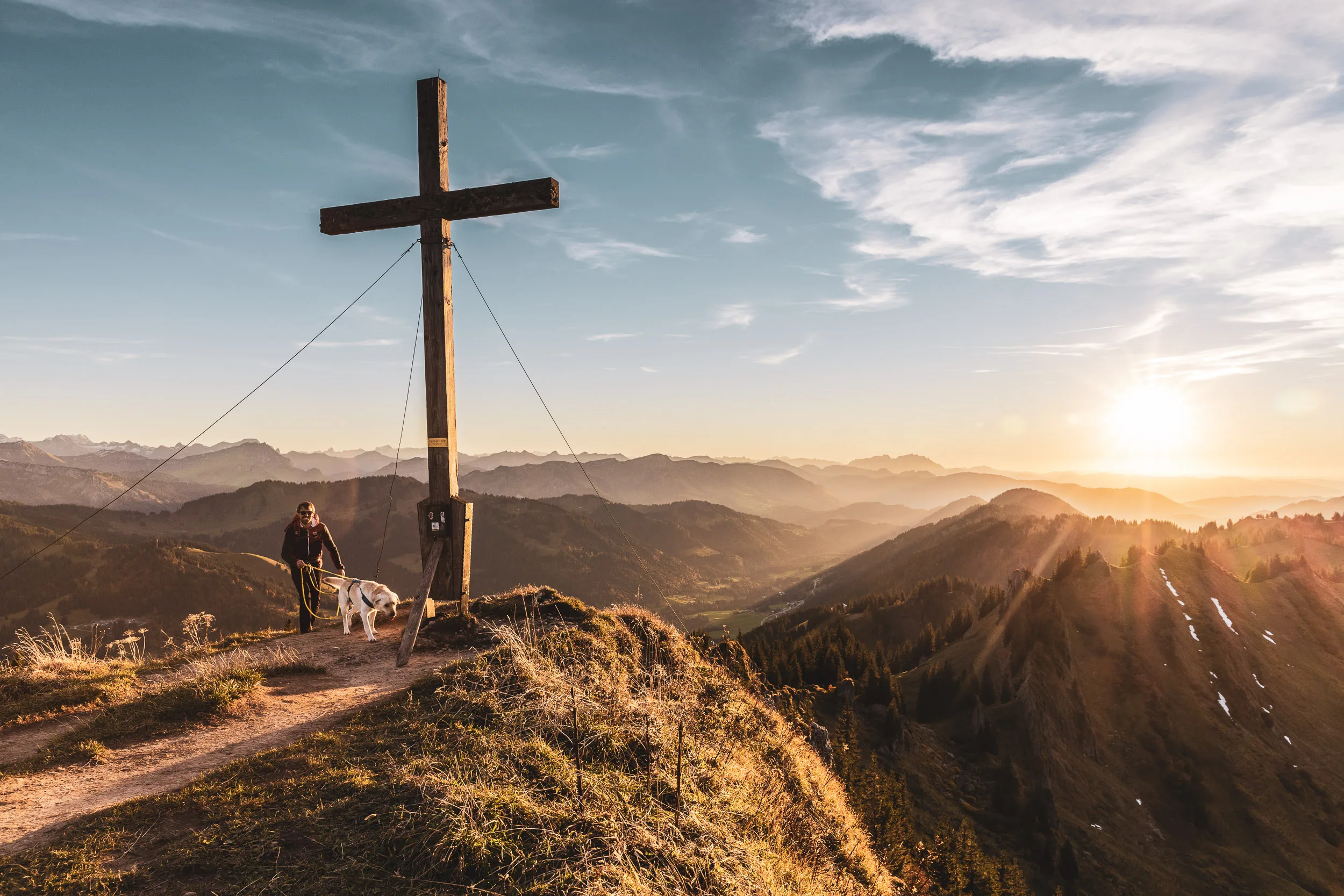 Andreas Kögel und Hund Oskar stehen am Gipfelkreuz über einem weiten Bergpanorama