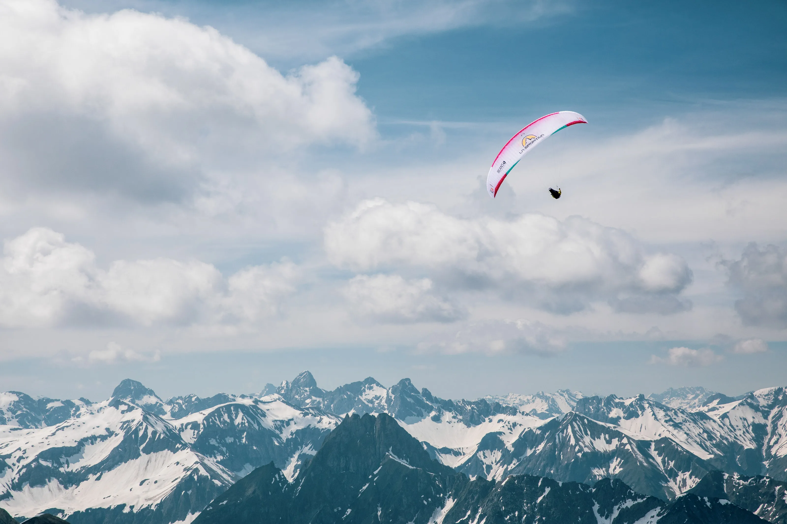 Michael Lacher hängt unter dem pinkweißen Schirm vor der schneebedeckten Alpenkette.