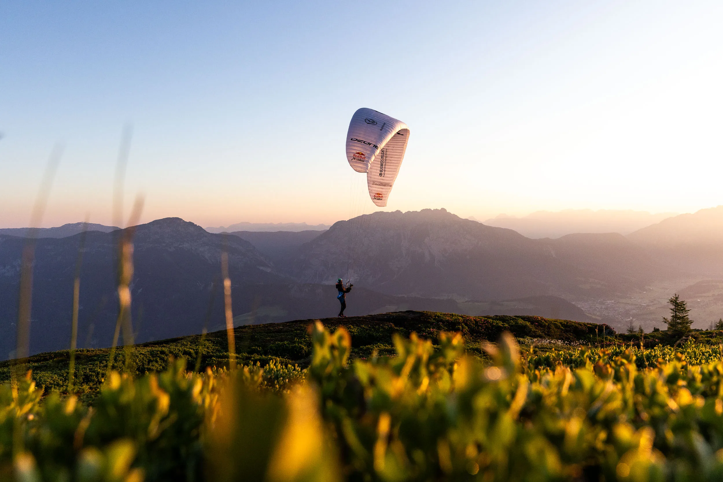 Gleitschirm ueber einer alpinen Wiese im Ennstal bei warmem Morgenlicht