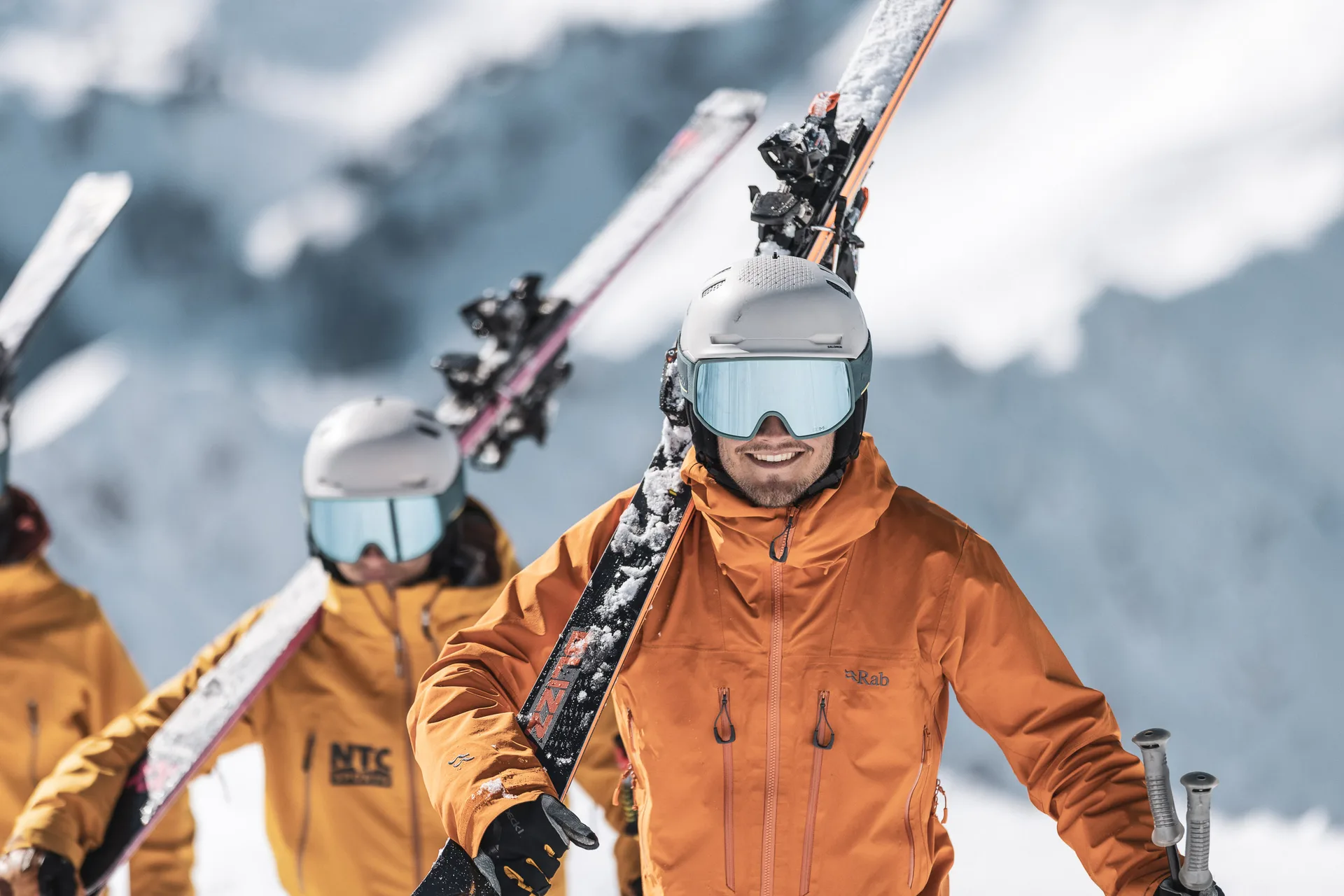 Skilehrer trägt Ski auf der Schulter, Kollegen folgen im Hintergrund