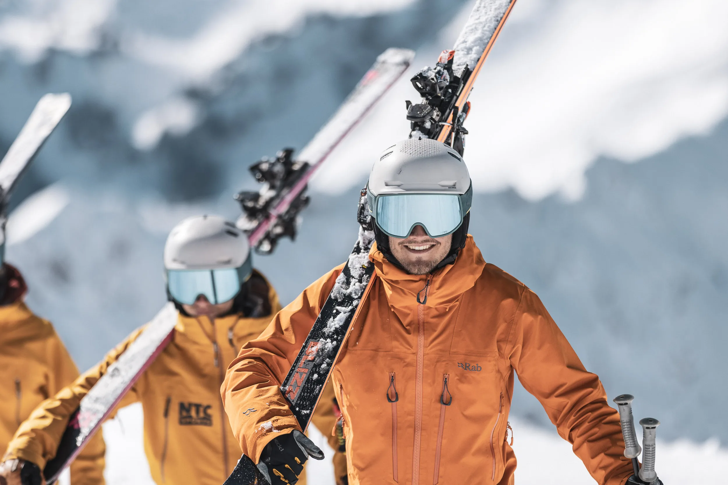 Skilehrer trägt Ski auf der Schulter, Kollegen folgen im Hintergrund