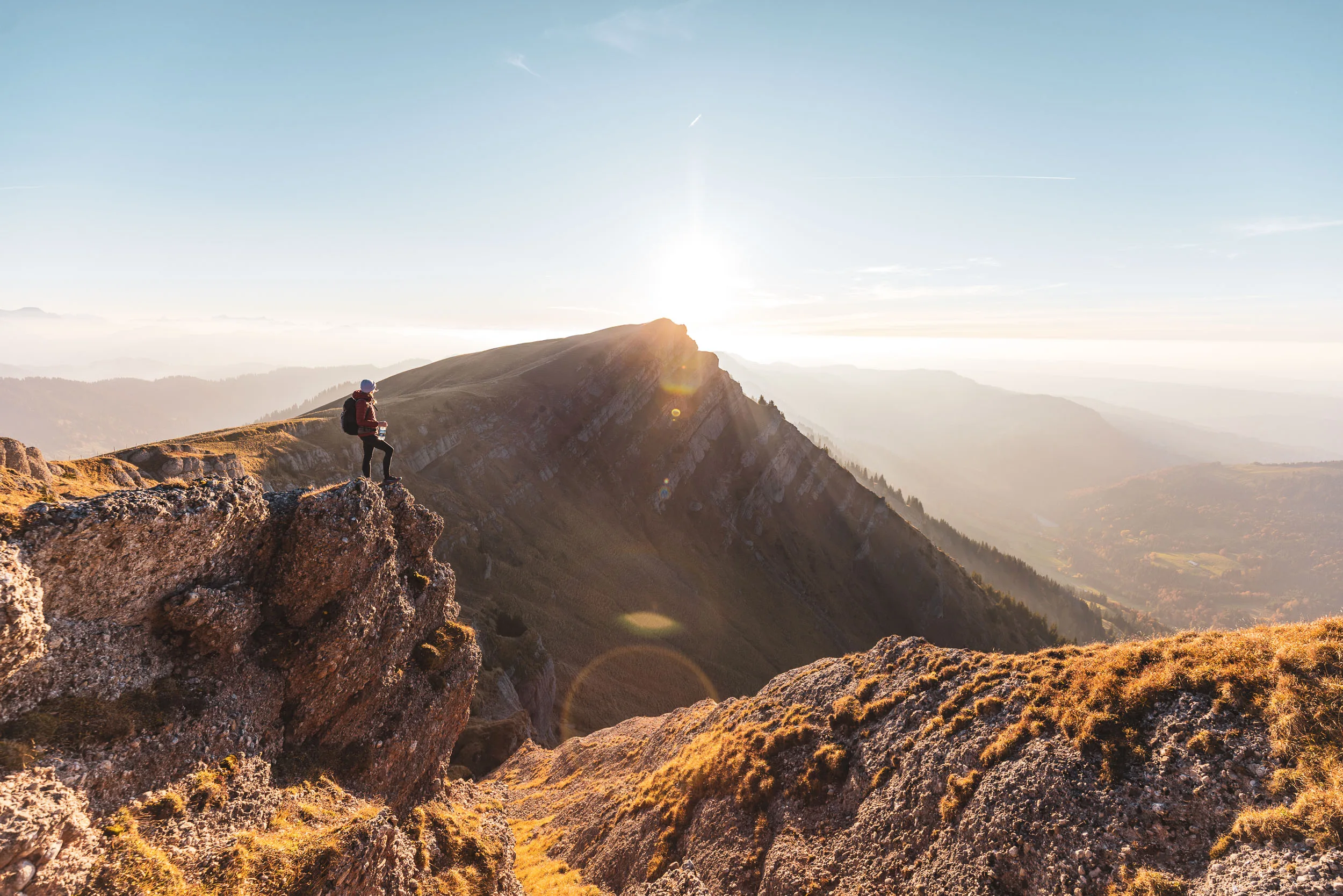 Wanderin steht auf einem Felsen und blickt auf den Grat und die Täler dahinter