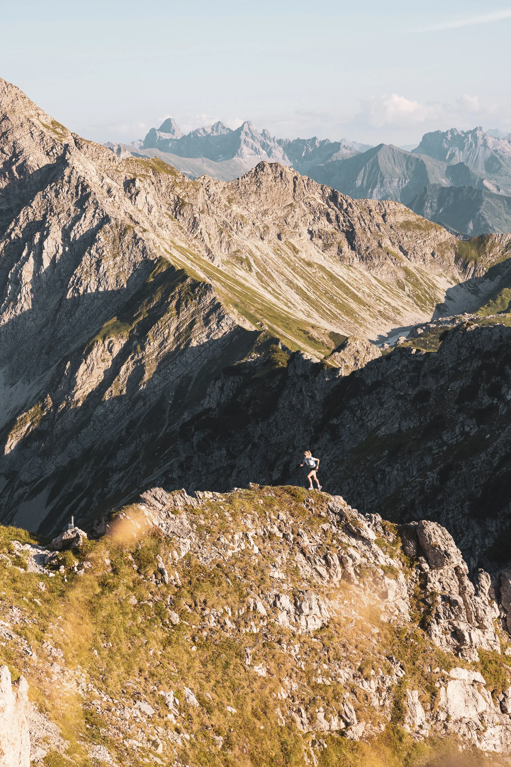 Kleine Trailrunnerin auf einem felsigen Grat vor weitem Alpenpanorama