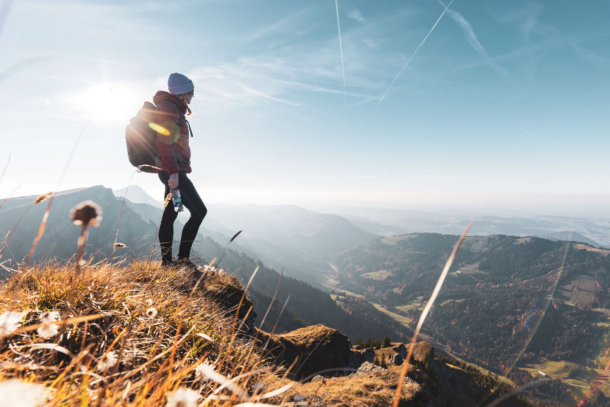 Wanderin steht im Gegenlicht auf einer kleinen Anhöhe über dem Tal