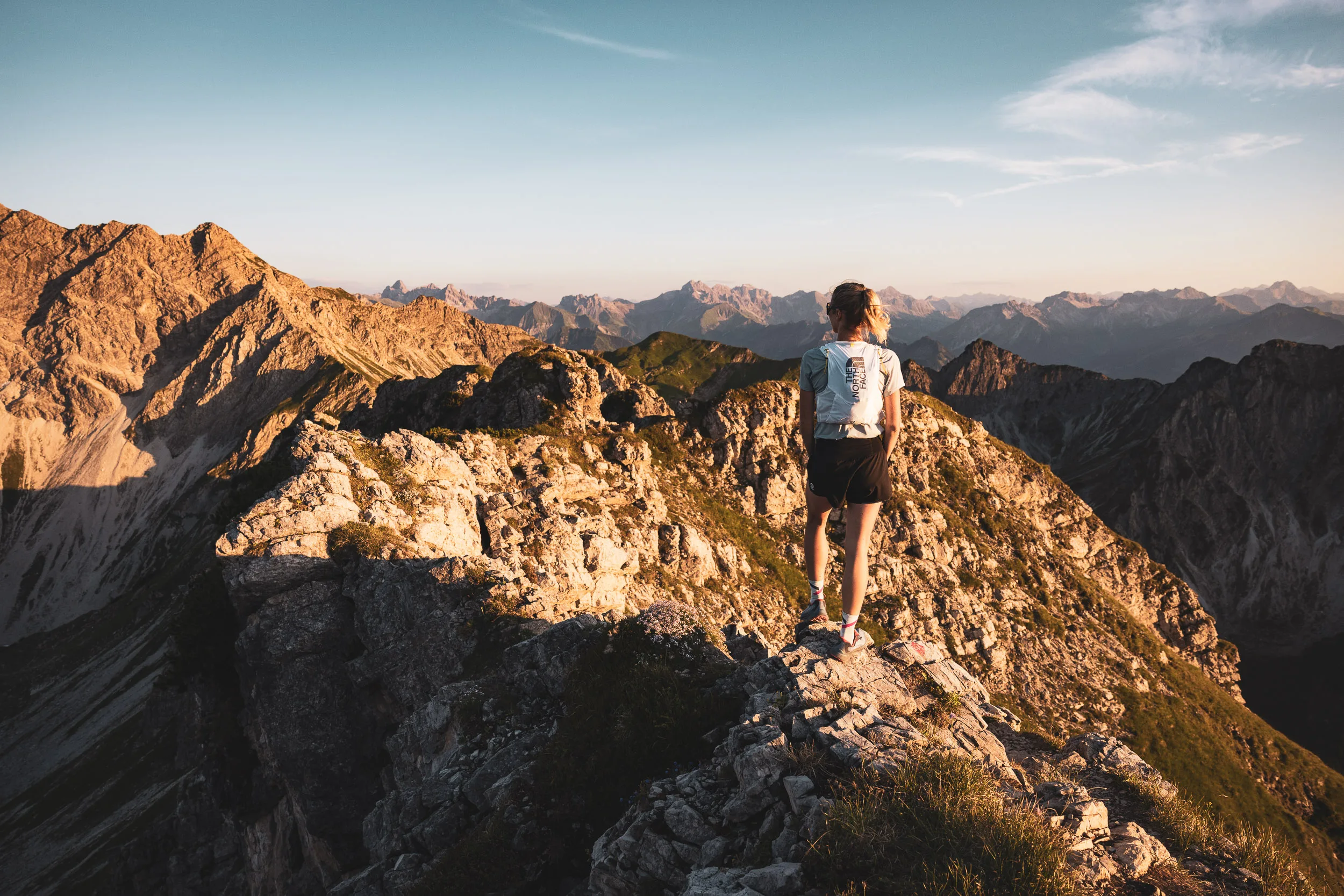 Läuferin steht im Abendlicht auf einem Felsen vor dem Alpenpanorama
