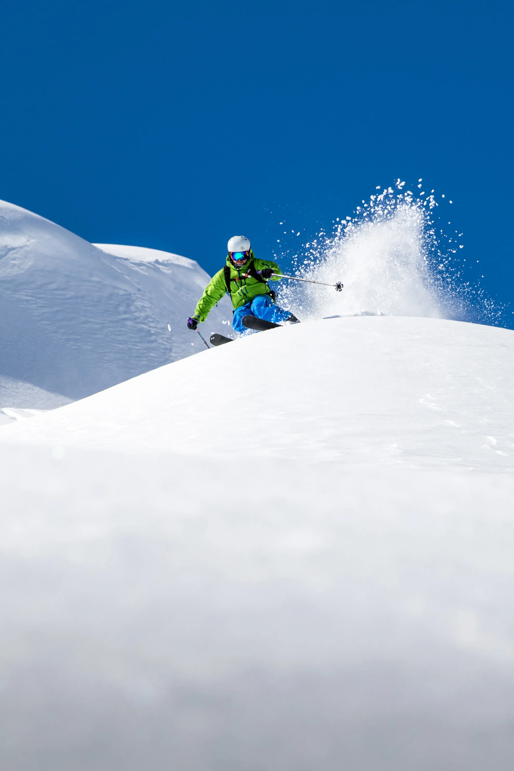 Skifahrer fährt durch Tiefschnee vor blauem Himmel.