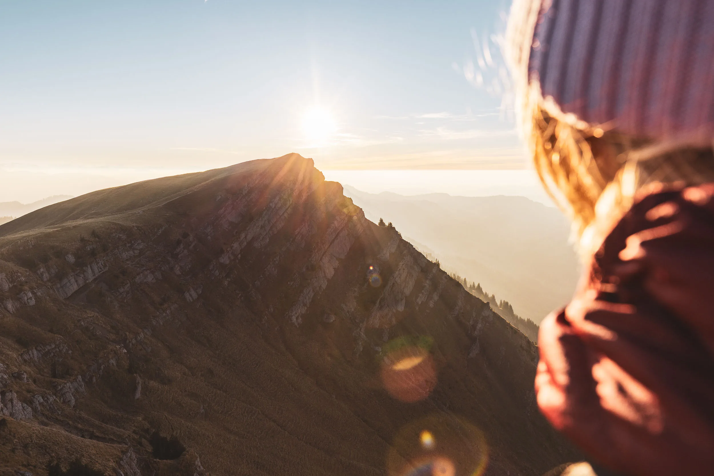 Wanderin steht nah im Vordergrund und blickt über den Grat in die Abendsonne