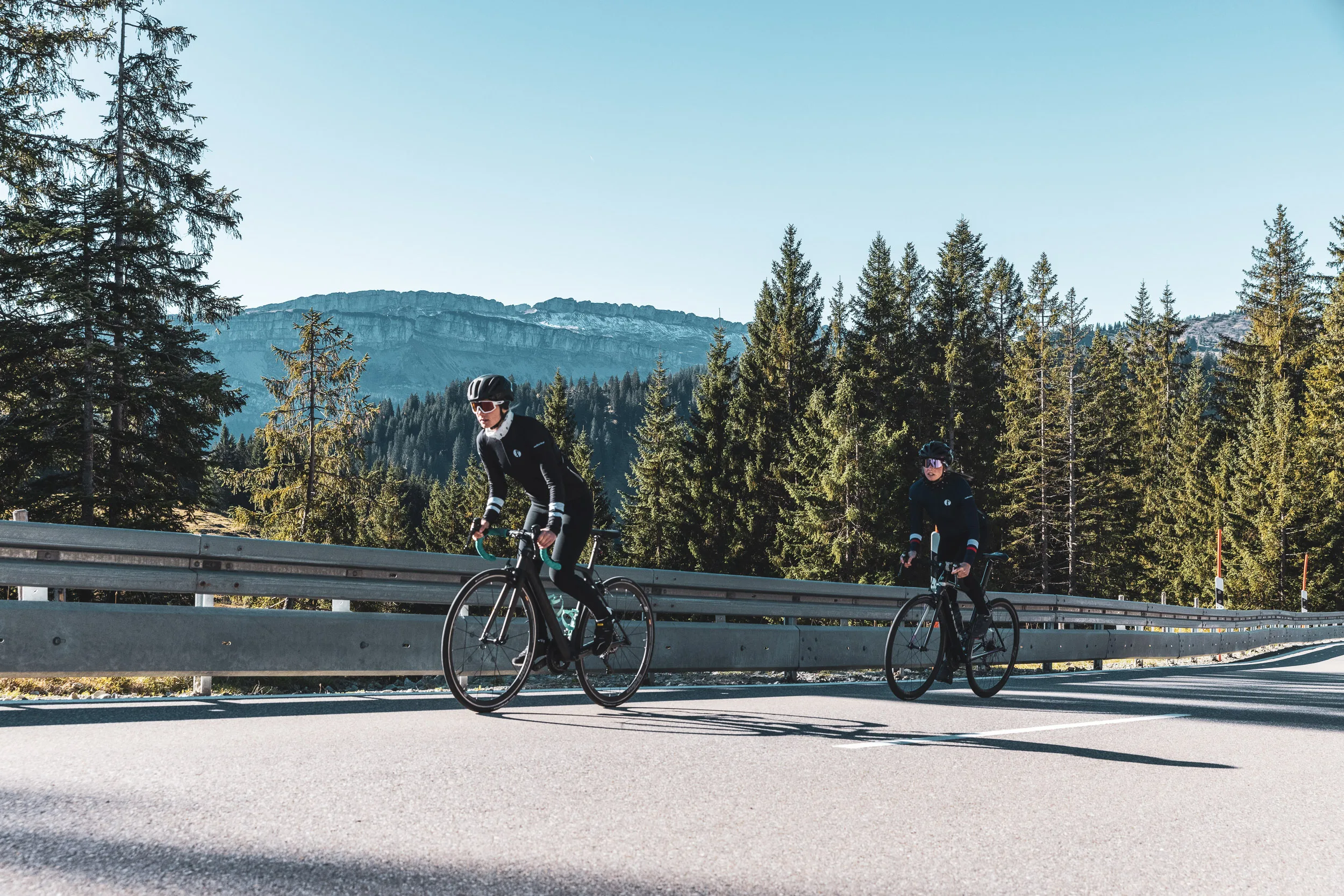 Zwei Rennradfahrerinnen auf einer ruhigen Passstraße im herbstlichen Allgäu
