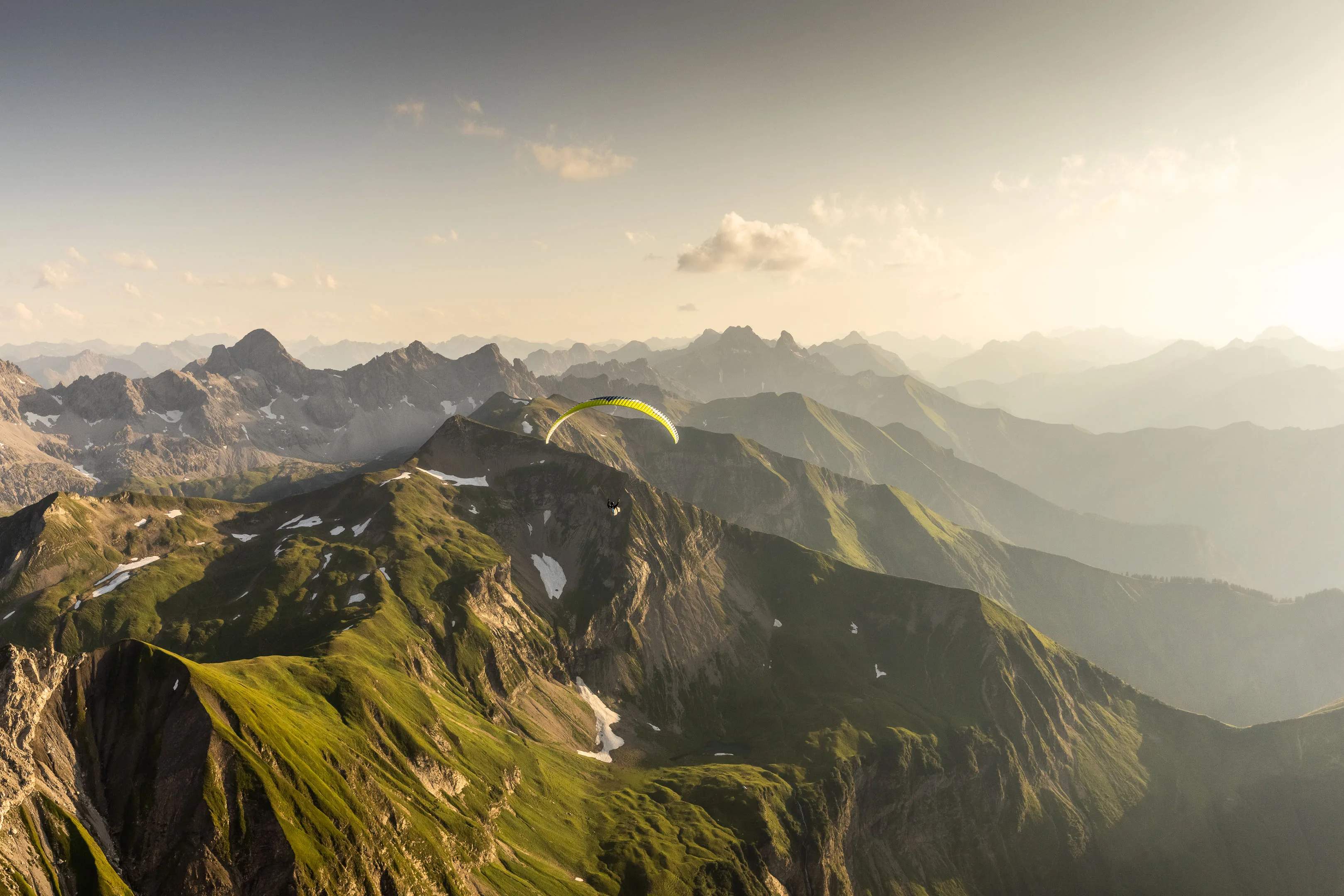 Ein Gleitschirm fliegt knapp über einem grünen Grat im letzten Sonnenlicht
