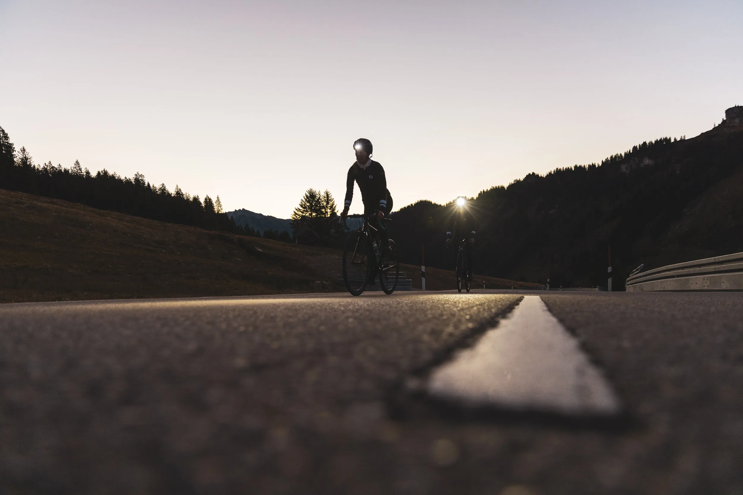 Rennradfahrerin fährt im tiefen Gegenlicht auf der Passstraße