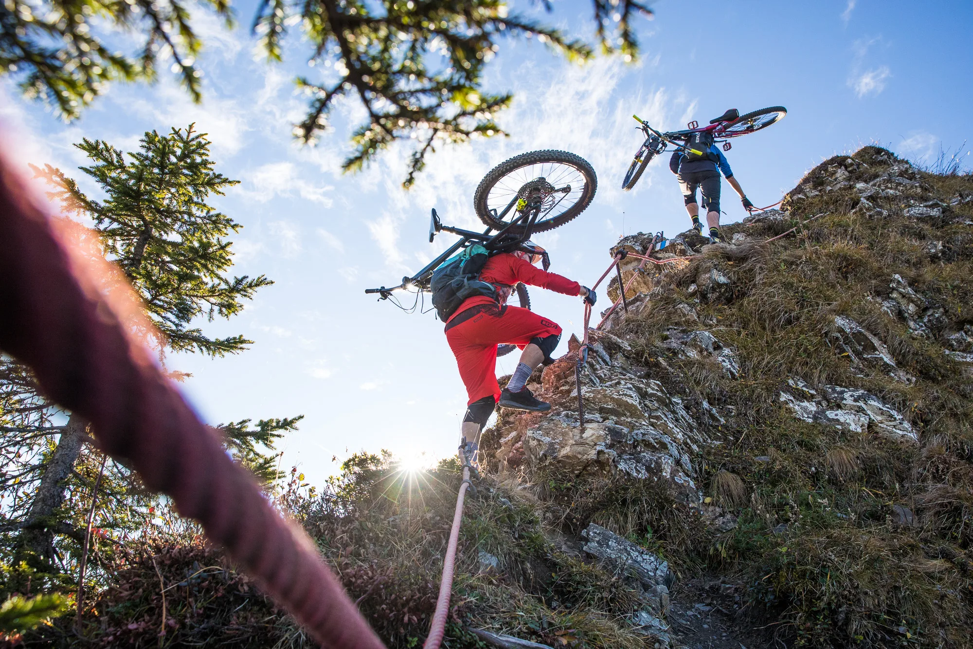 Zwei Mountainbiker tragen ihre Räder an einem felsigen Steilhang nach oben