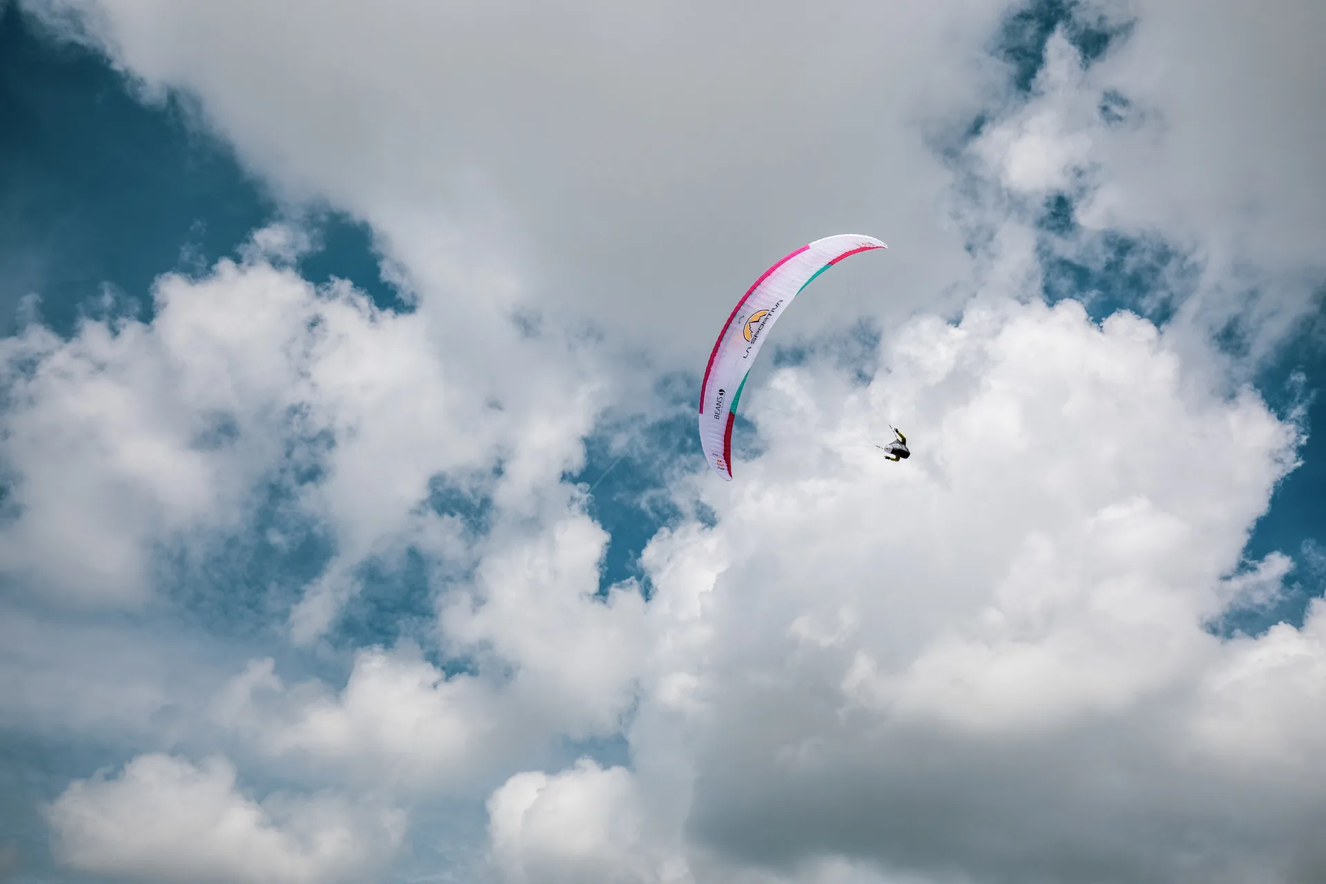 Michael Lacher fliegt unter dem pinkweißen Schirm vor aufgelockerten Wolken.