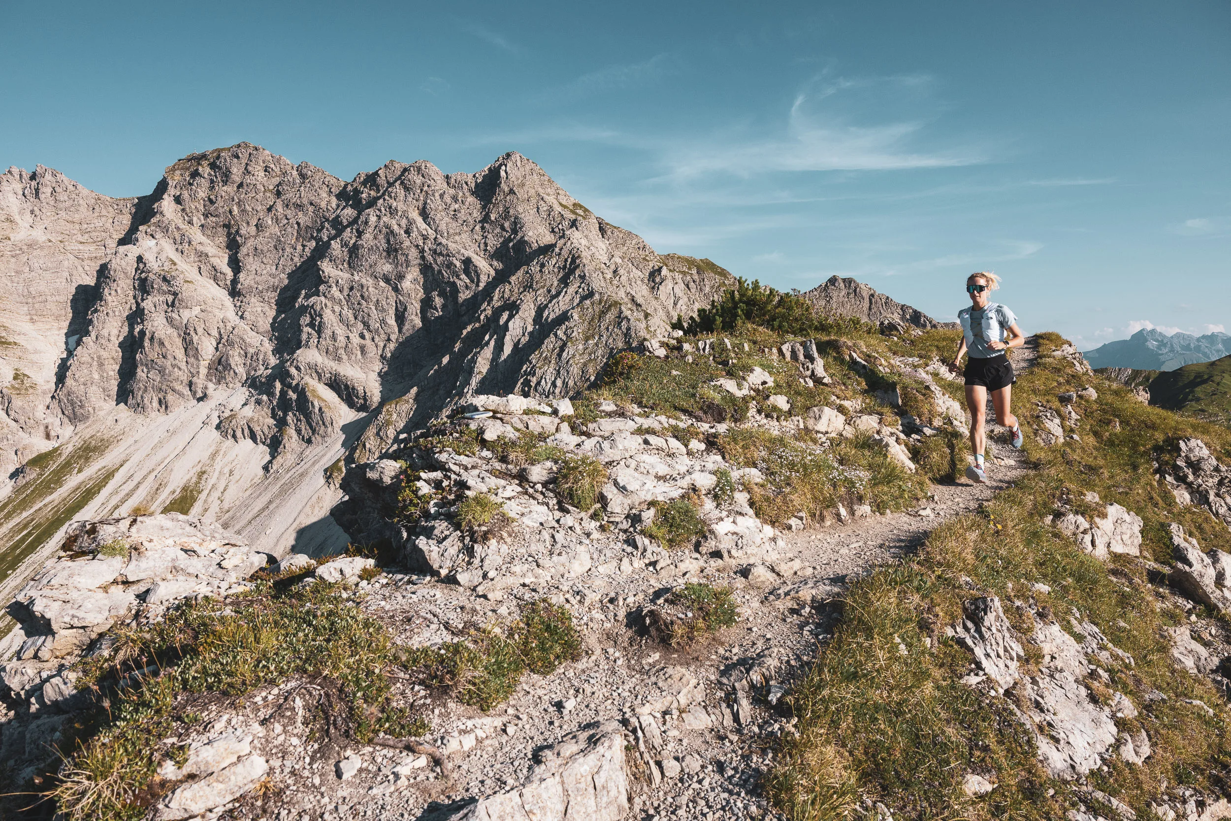 Trailrunnerin auf einem steinigen Grat zwischen Gras und Fels