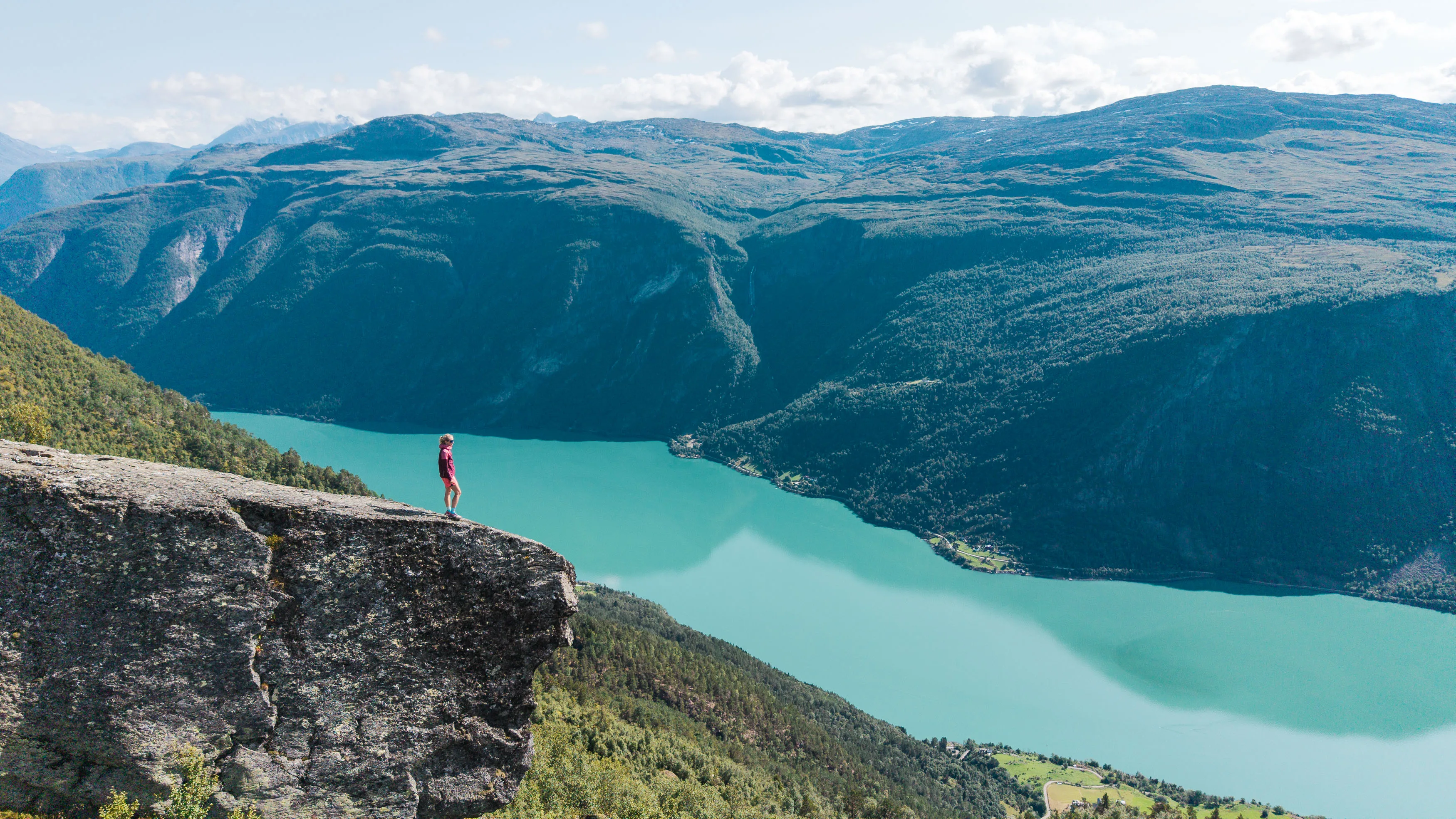 Person steht auf einem Felsvorsprung hoch über einem türkisfarbenen Bergsee