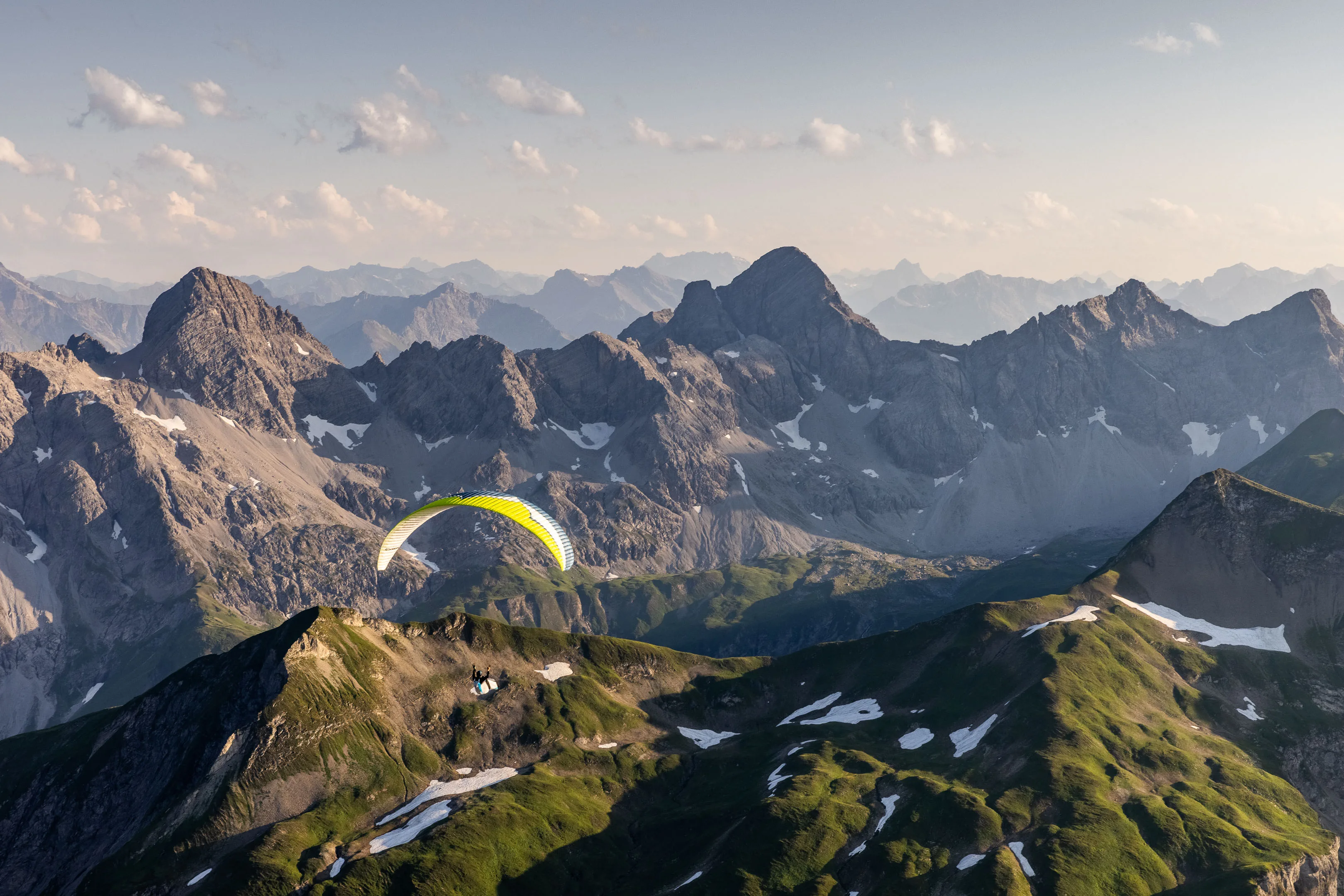 Michael Schnetzer fliegt vor dunklen Felsspitzen über einen grünen Bergkamm