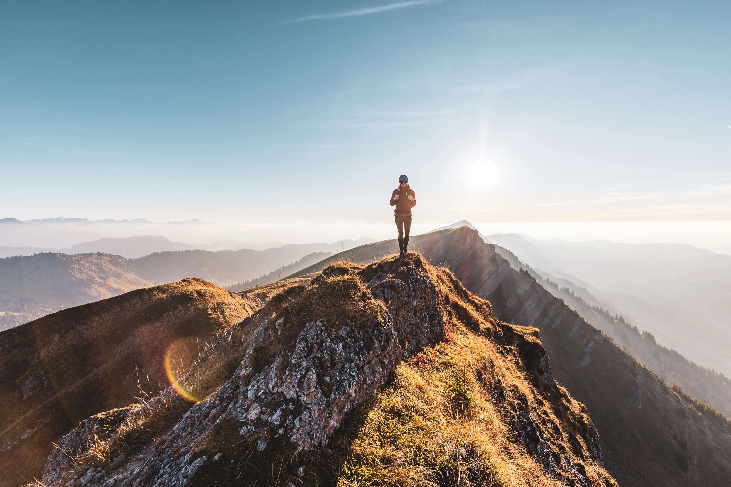 Wanderin steht als Silhouette auf einem Felsen direkt vor der tiefen Sonne