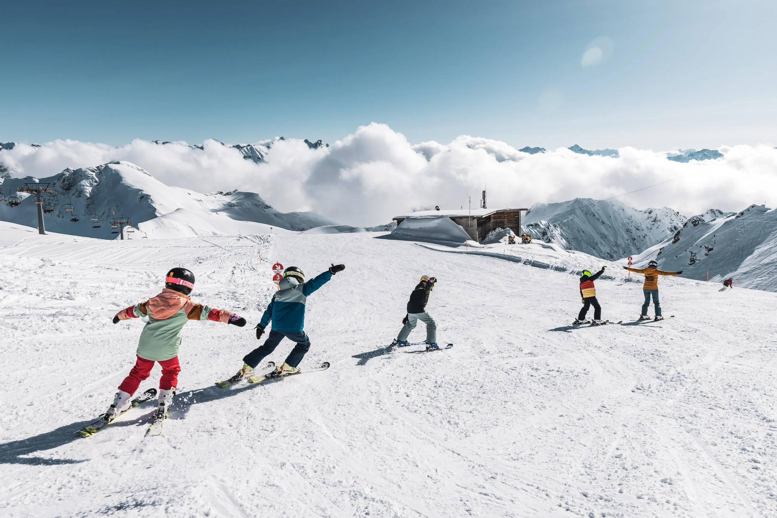Kinder üben mit Skilehrern Kurven auf breiter Piste am Nebelhorn
