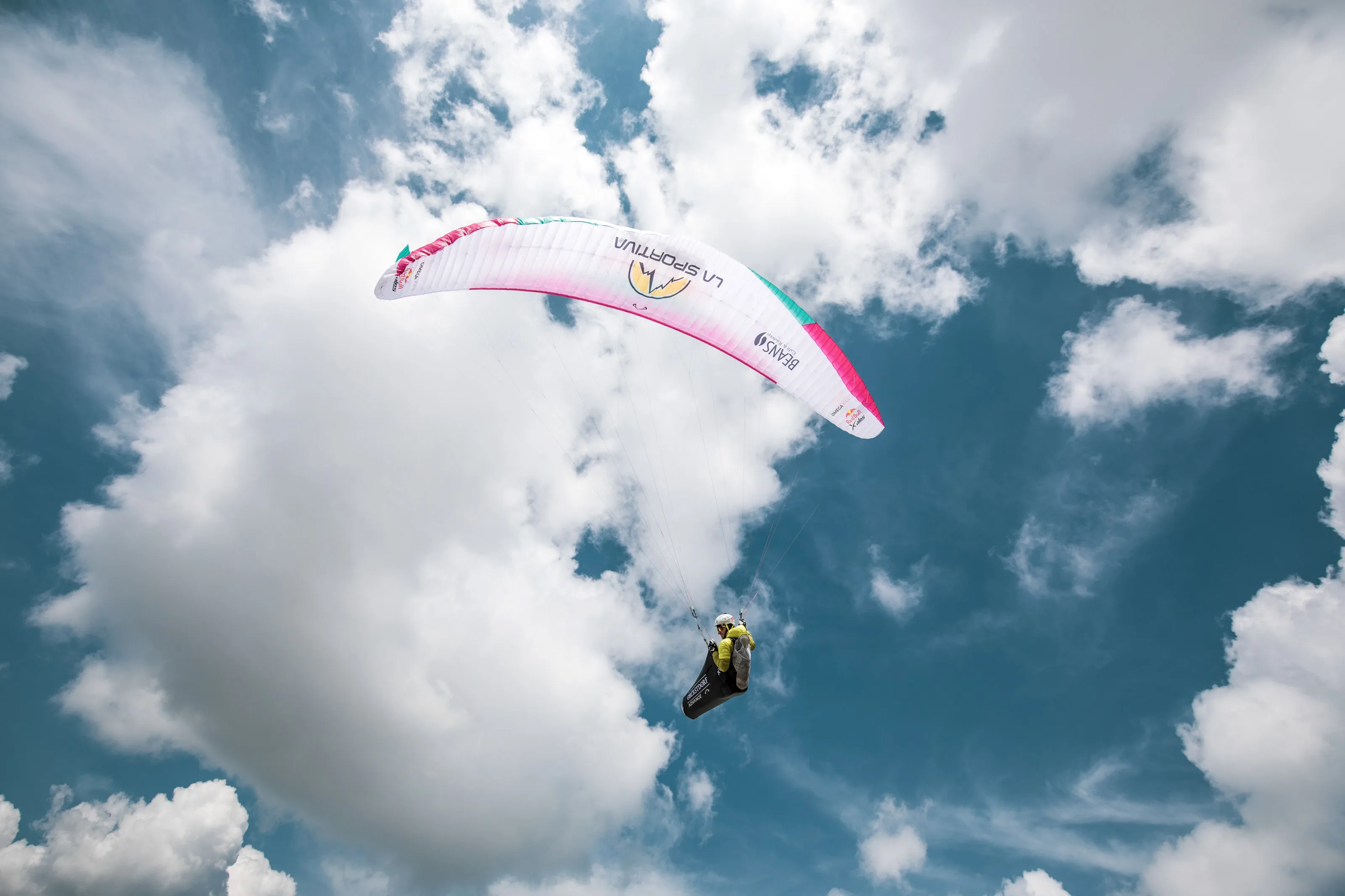 Ein nah fotografierter pinkweißer Gleitschirm füllt den Himmel über Michael Lacher und dem Berggrat.