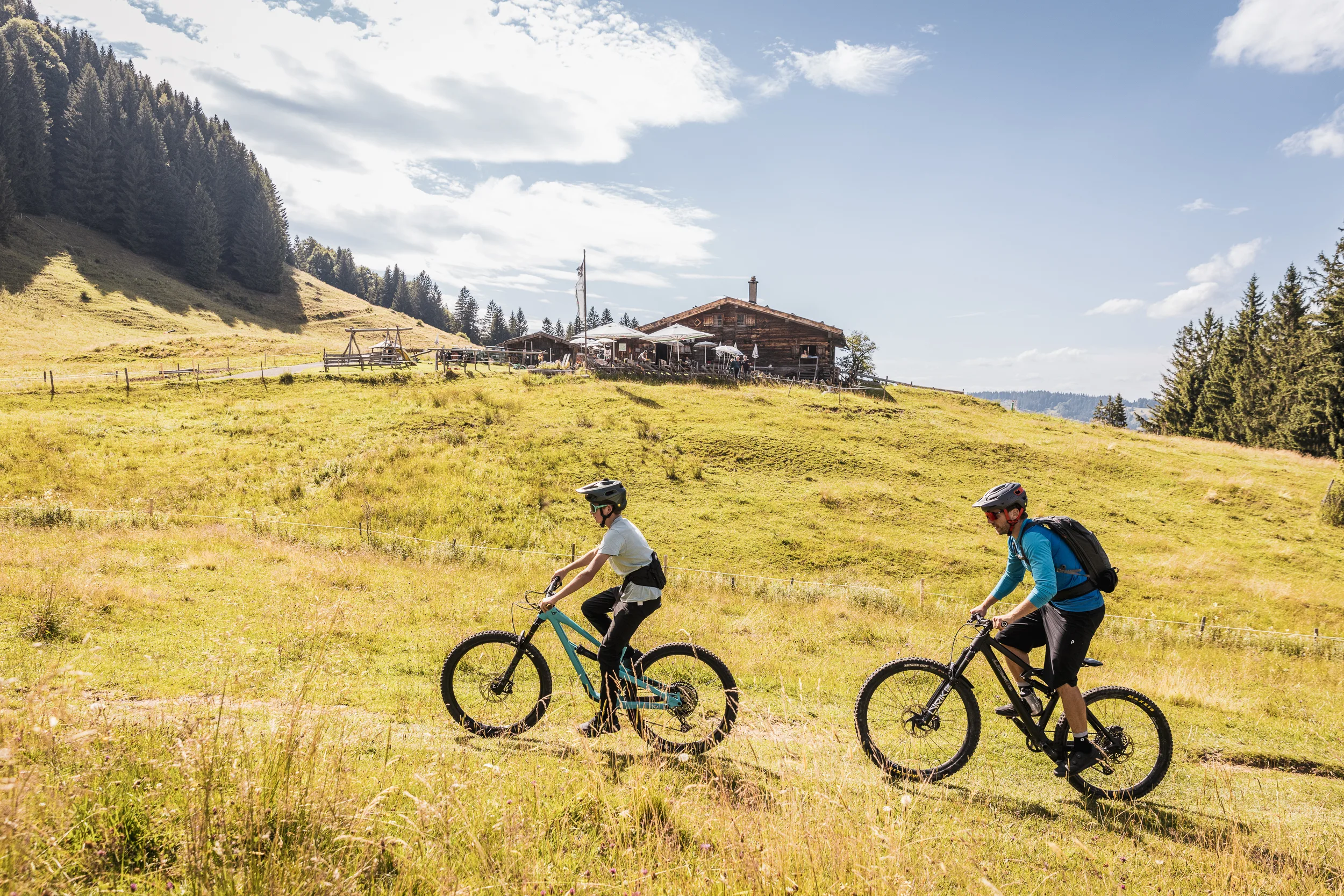 Zwei Mountainbiker fahren hintereinander durch eine offene Allgäuer Bergwiese