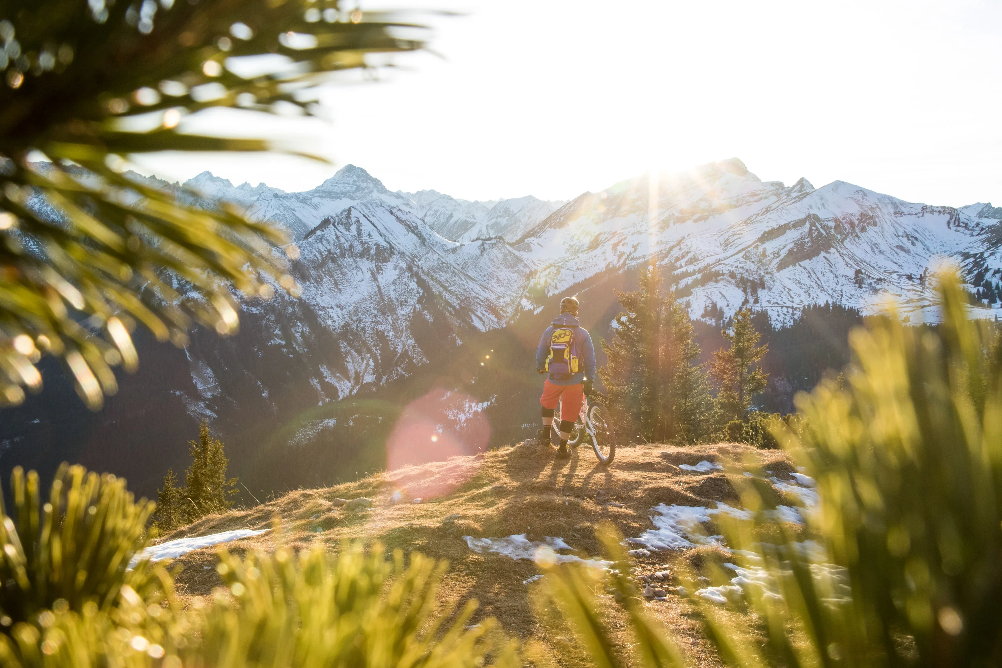 Florian Bergmann sitzt neben seinem Mountainbike mit Blick auf verschneite Berge.