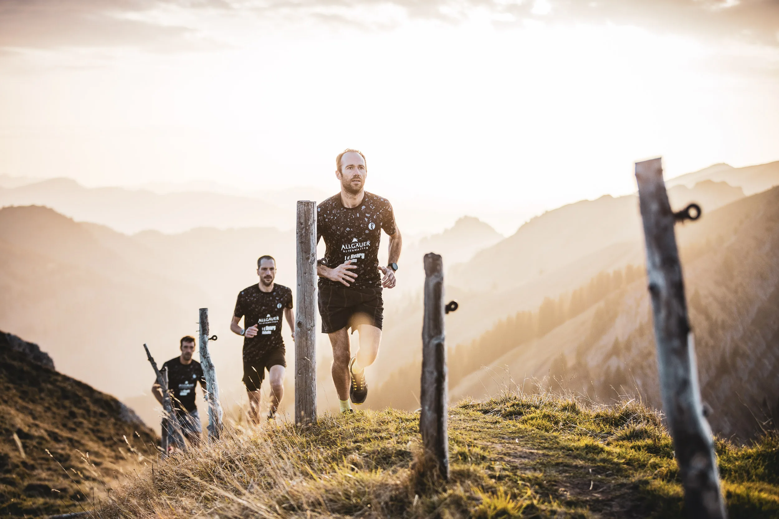 Trailrunner laufen zwischen Holzpfosten auf einem Gratweg bergauf