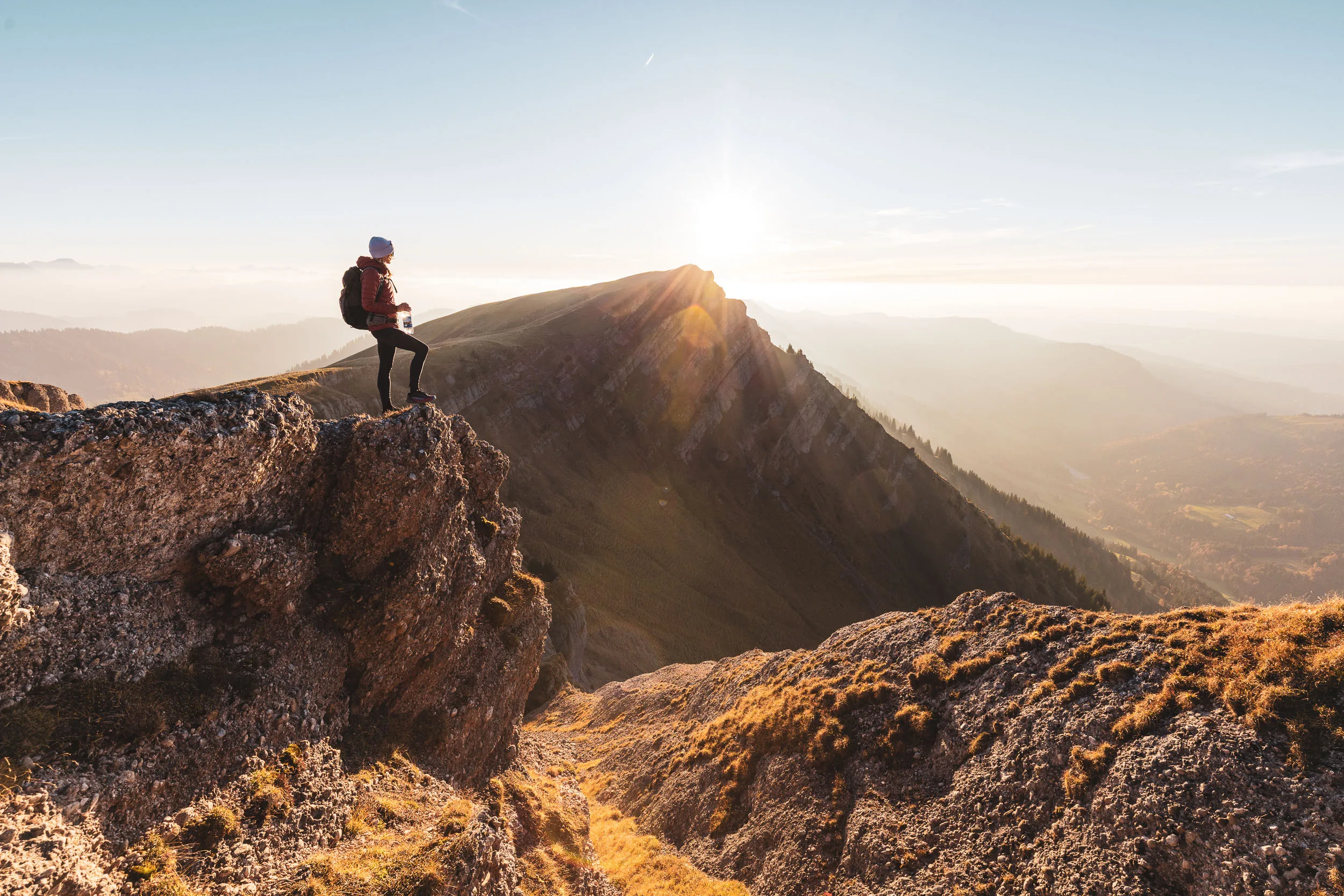Wanderin steht allein auf einem Felsvorsprung vor dem steilen Bergkamm