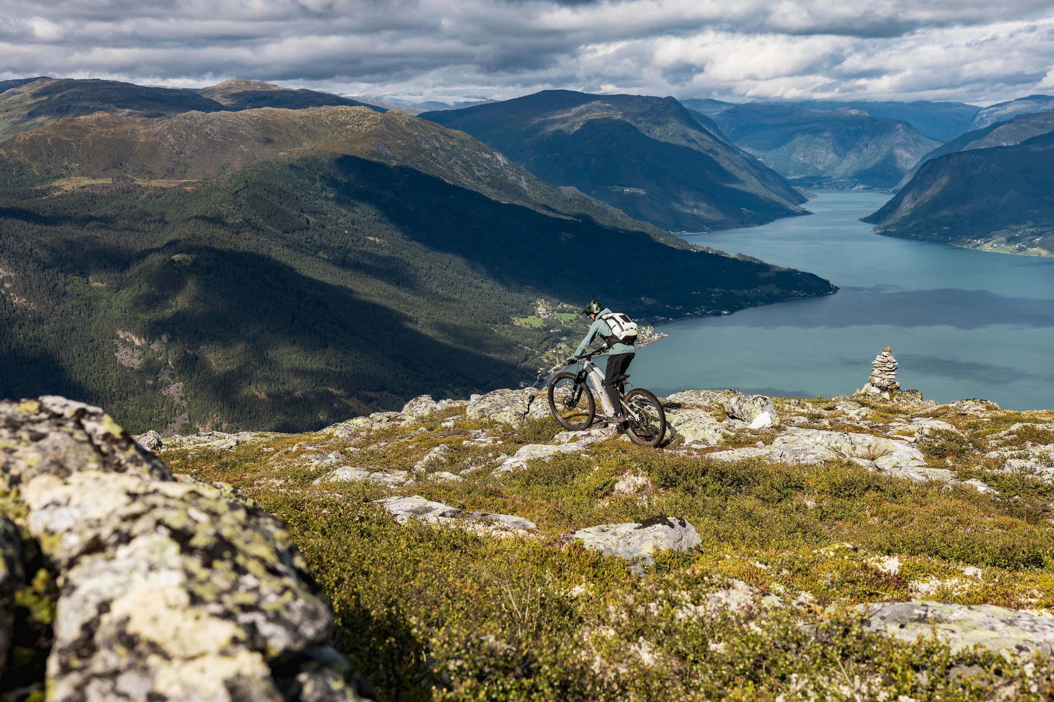 Mountainbiker folgt einem felsigen Höhenweg mit einem langgestreckten Fjord im Hintergrund