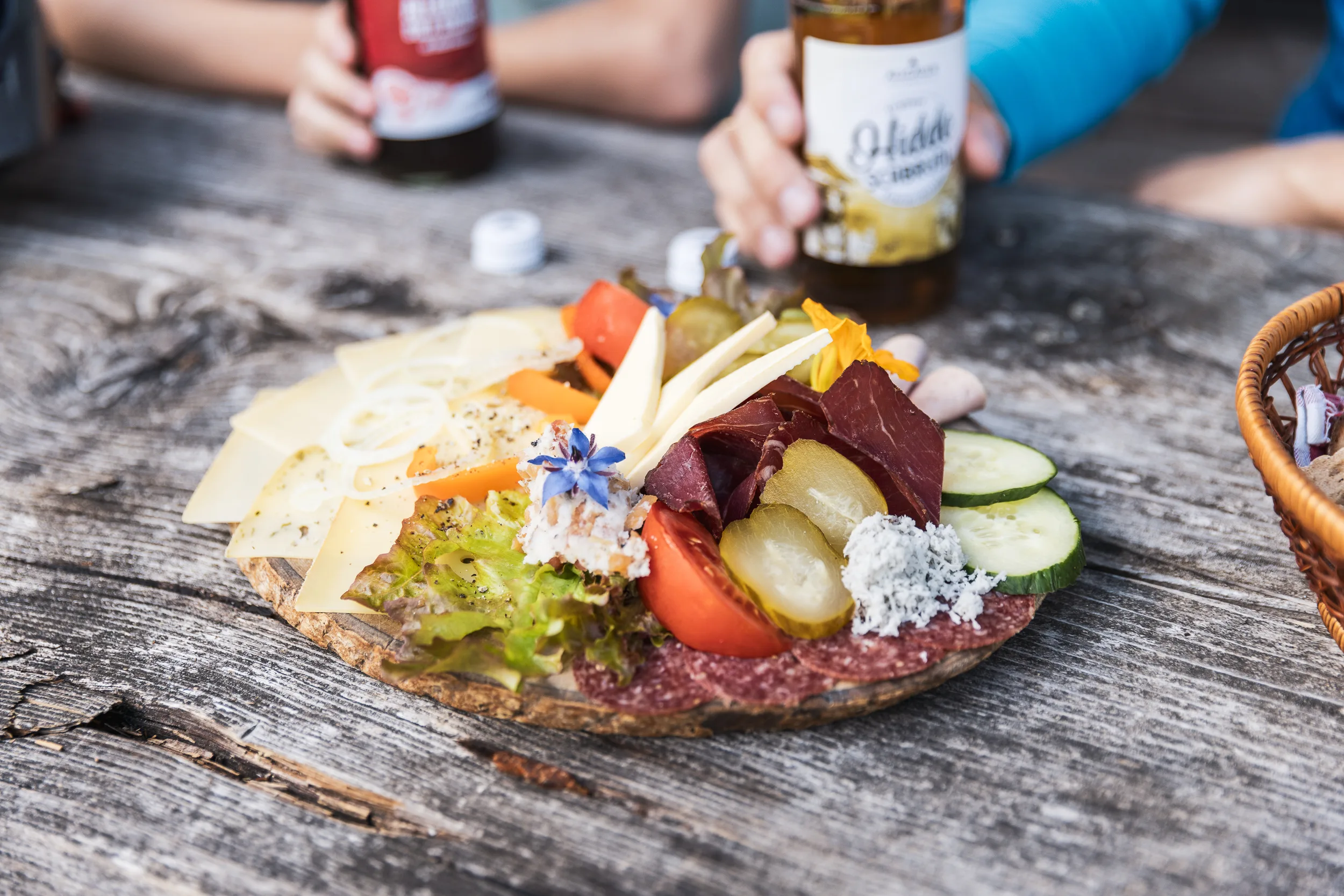 Brotzeitbrett mit Käse, Gemüse und Getränk auf dem Holztisch der Alpe