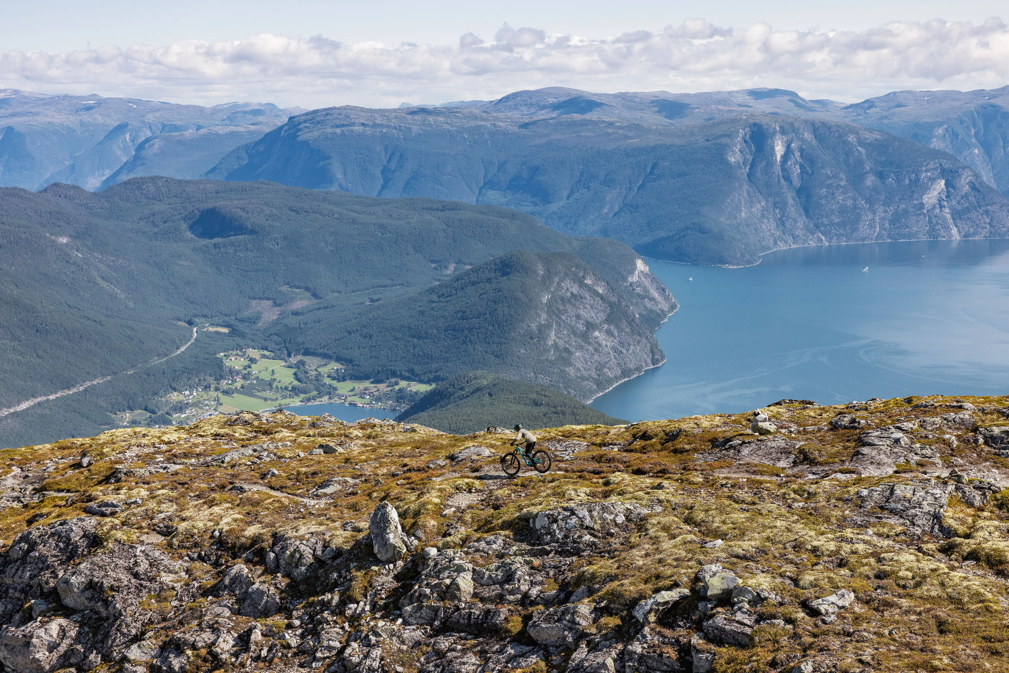 Mountainbiker quert einen felsigen Höhenweg vor steilen Fjordhängen