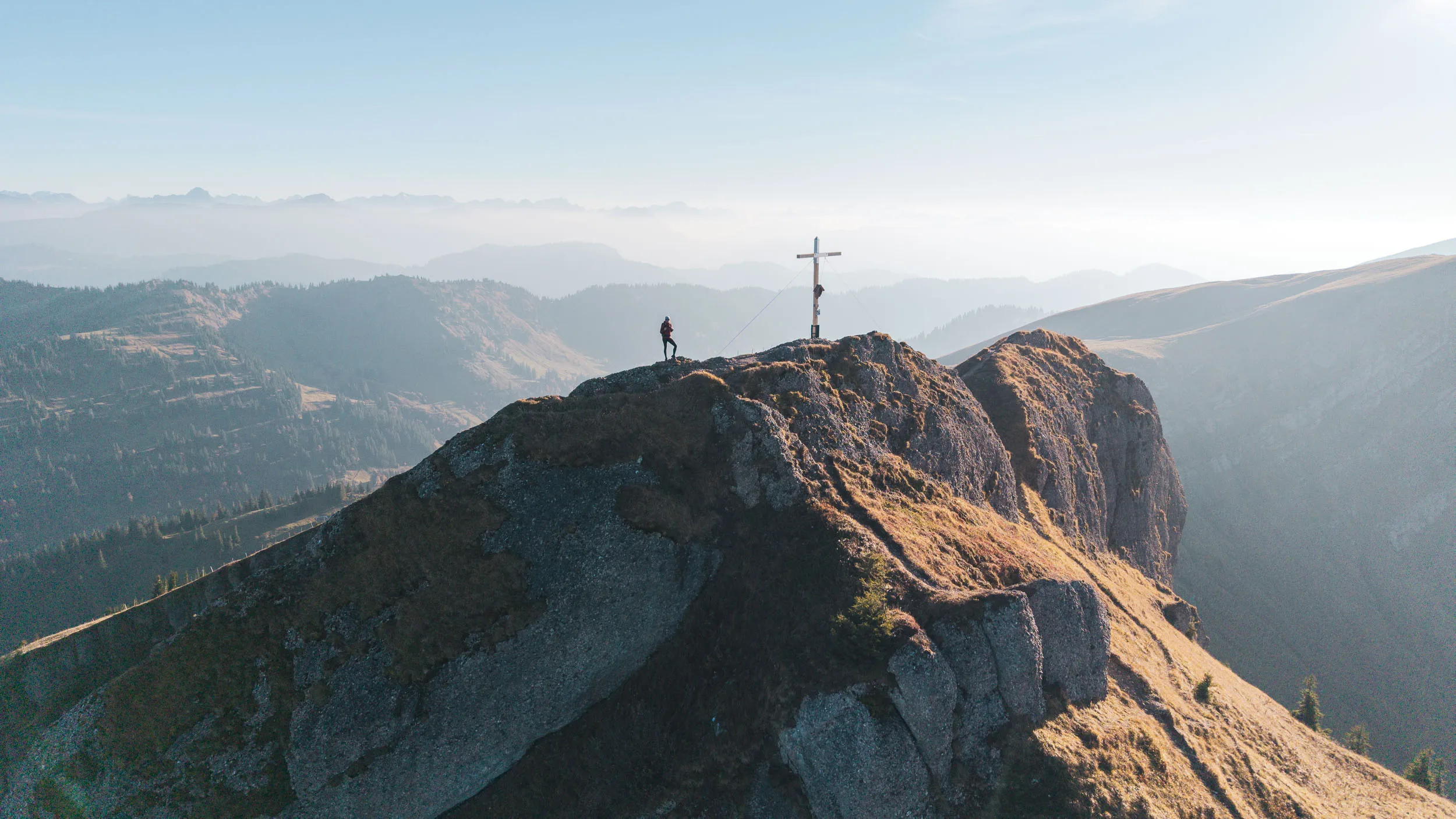 Kleine Wanderin steht neben einem Gipfelkreuz vor gestaffelten Allgäuer Bergketten