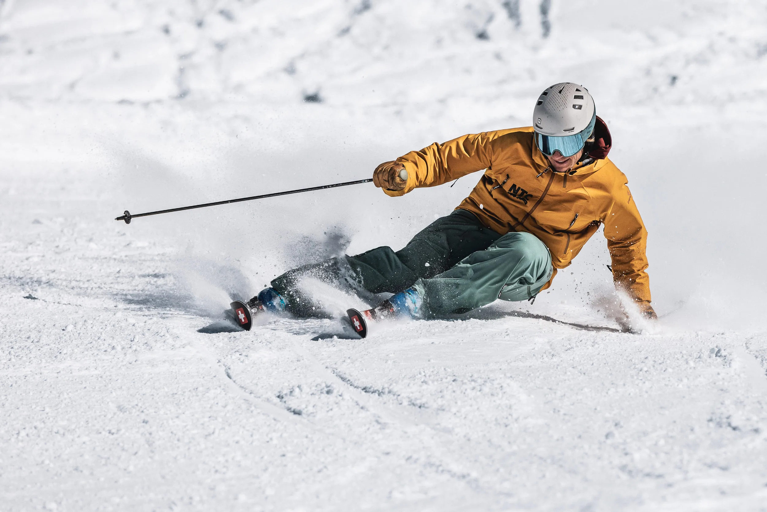 Skilehrer carvt mit ausgestrecktem Arm über die Piste