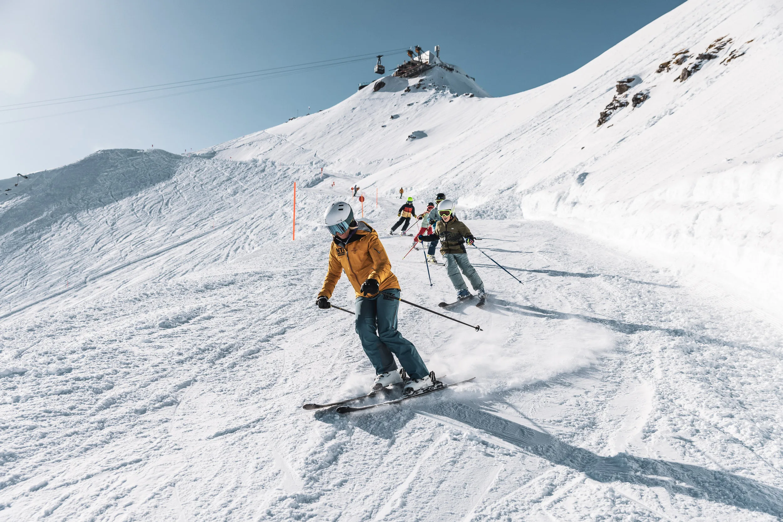 Skilehrer führt eine Gruppe in kurzen Schwüngen über die Piste