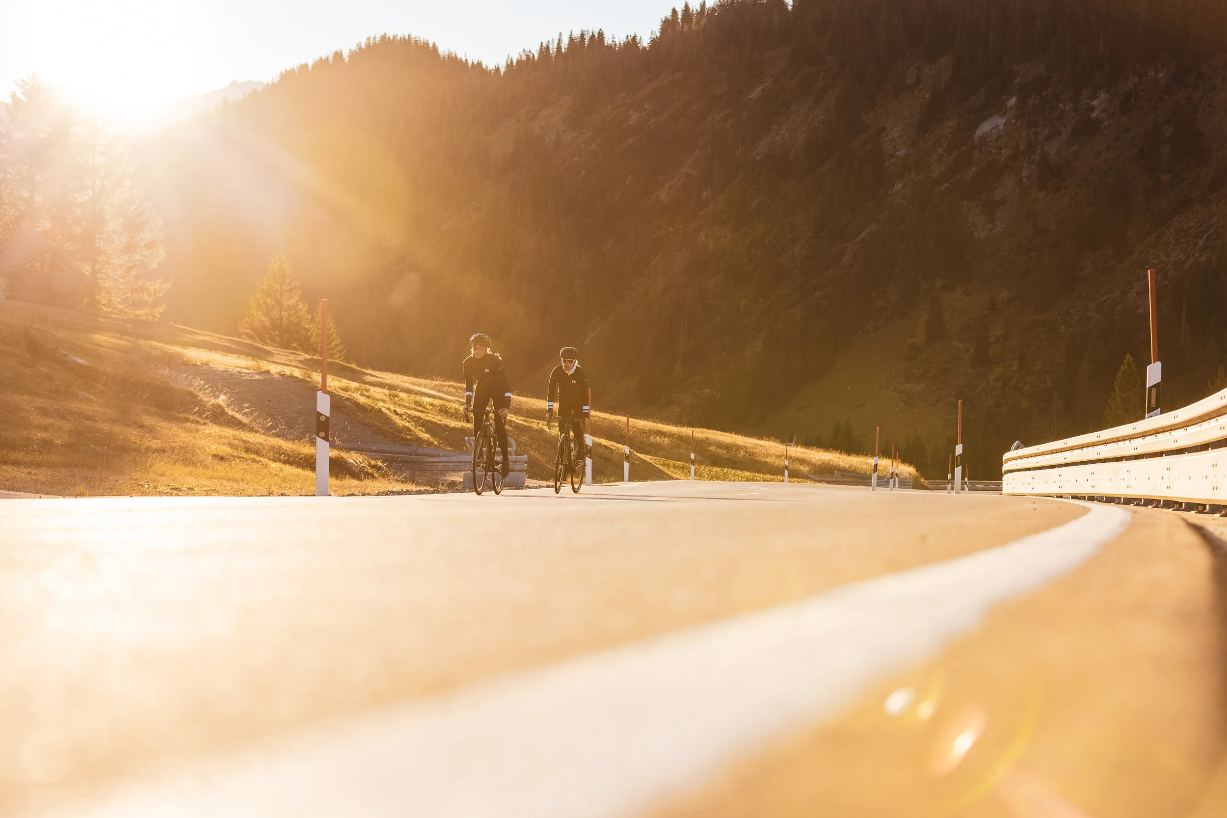 Zwei Rennradfahrerinnen nähern sich über eine Passstraße im Gegenlicht