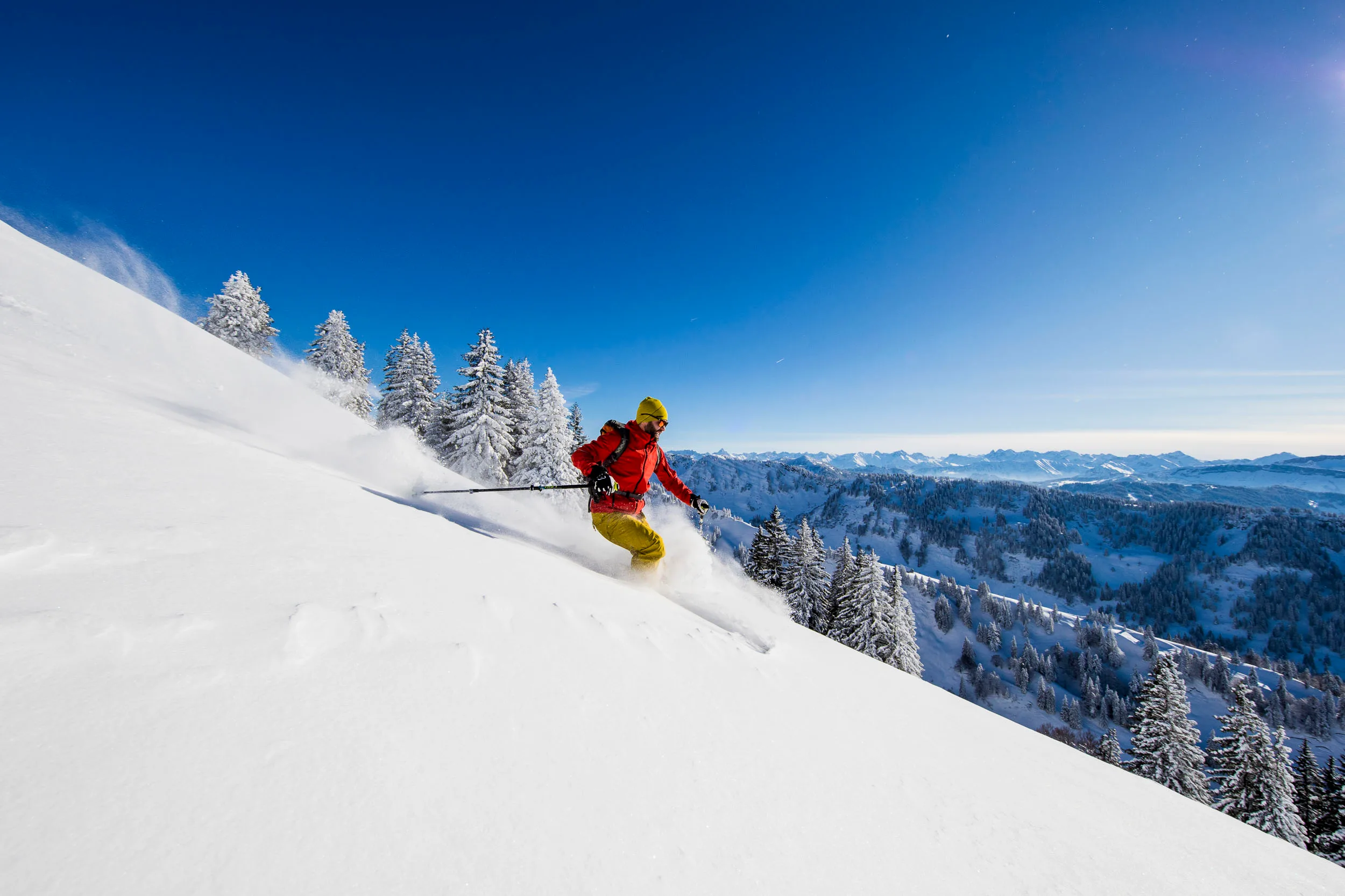 Skifahrer zieht im Pulverschnee eine breite Spur unter klarem Himmel.