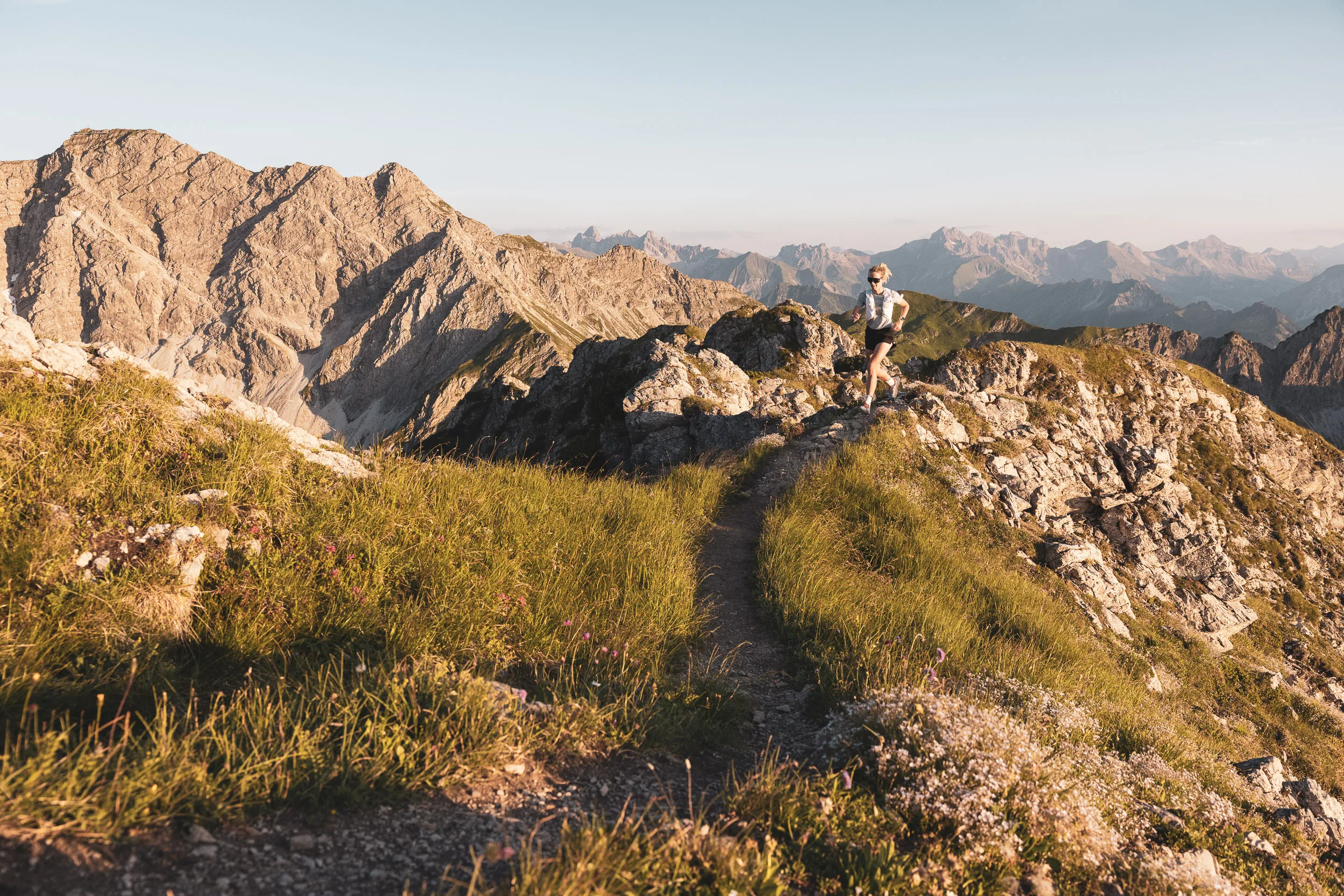 Trailrunnerin auf einem geschwungenen Bergpfad zwischen Gras und Fels