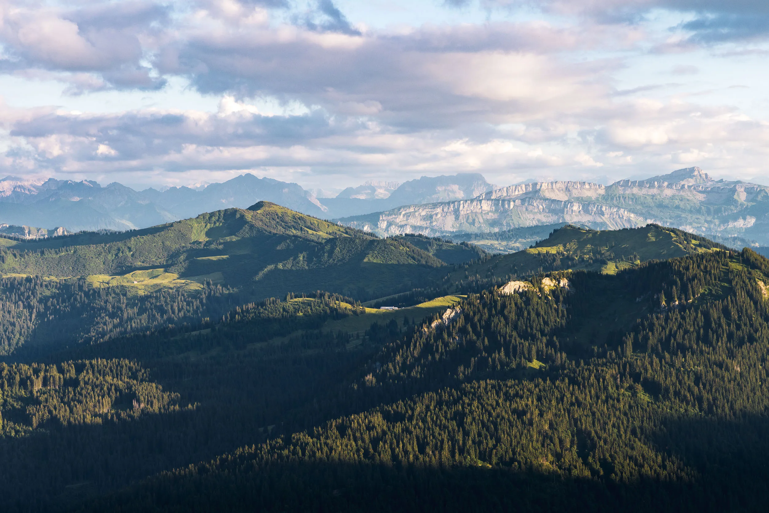 Wolken ziehen über helle Felswände und grüne, bewaldete Bergrücken im Allgäu.