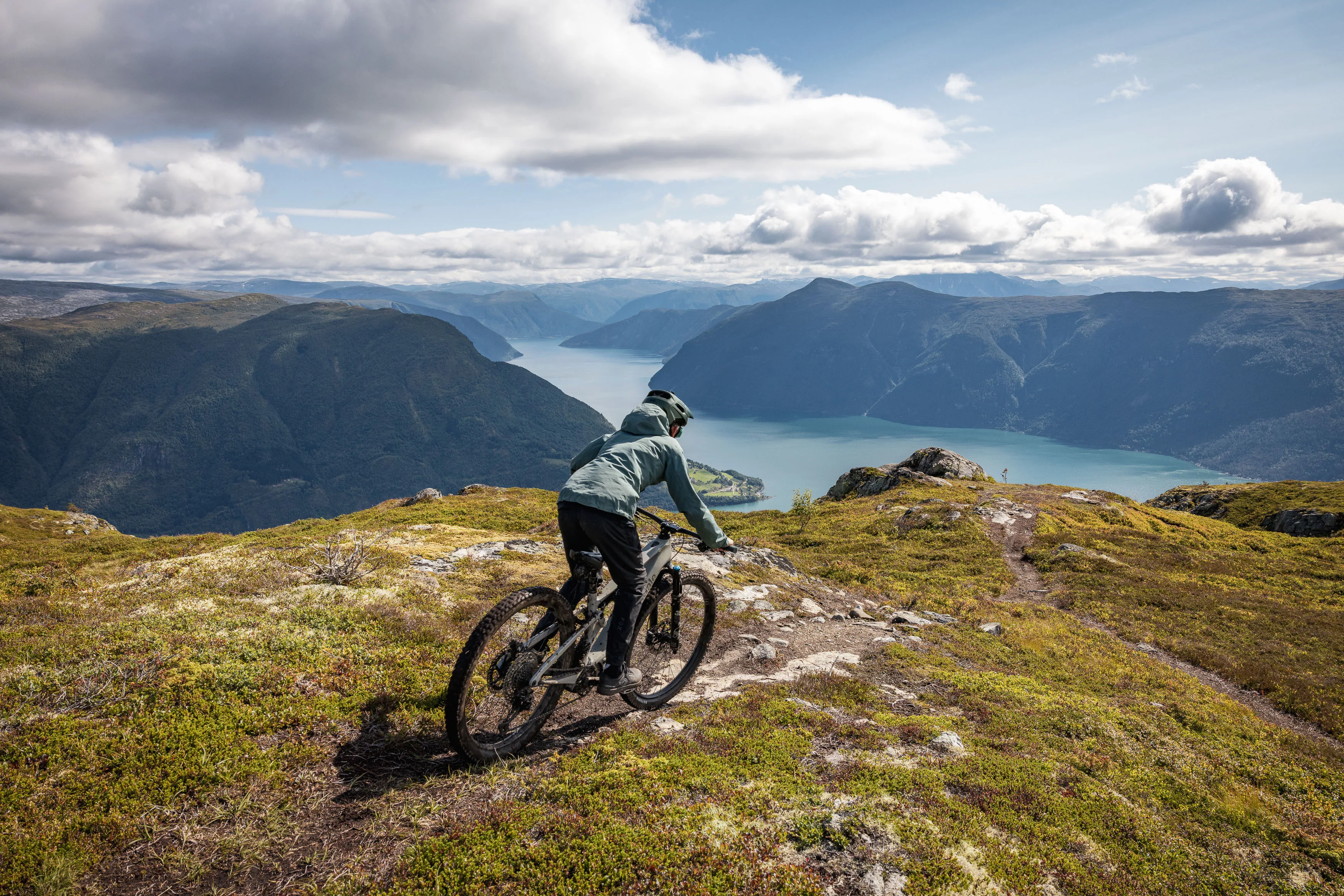 Mountainbiker legt sich auf einem schmalen Höhenweg über dem Fjord in die Kurve