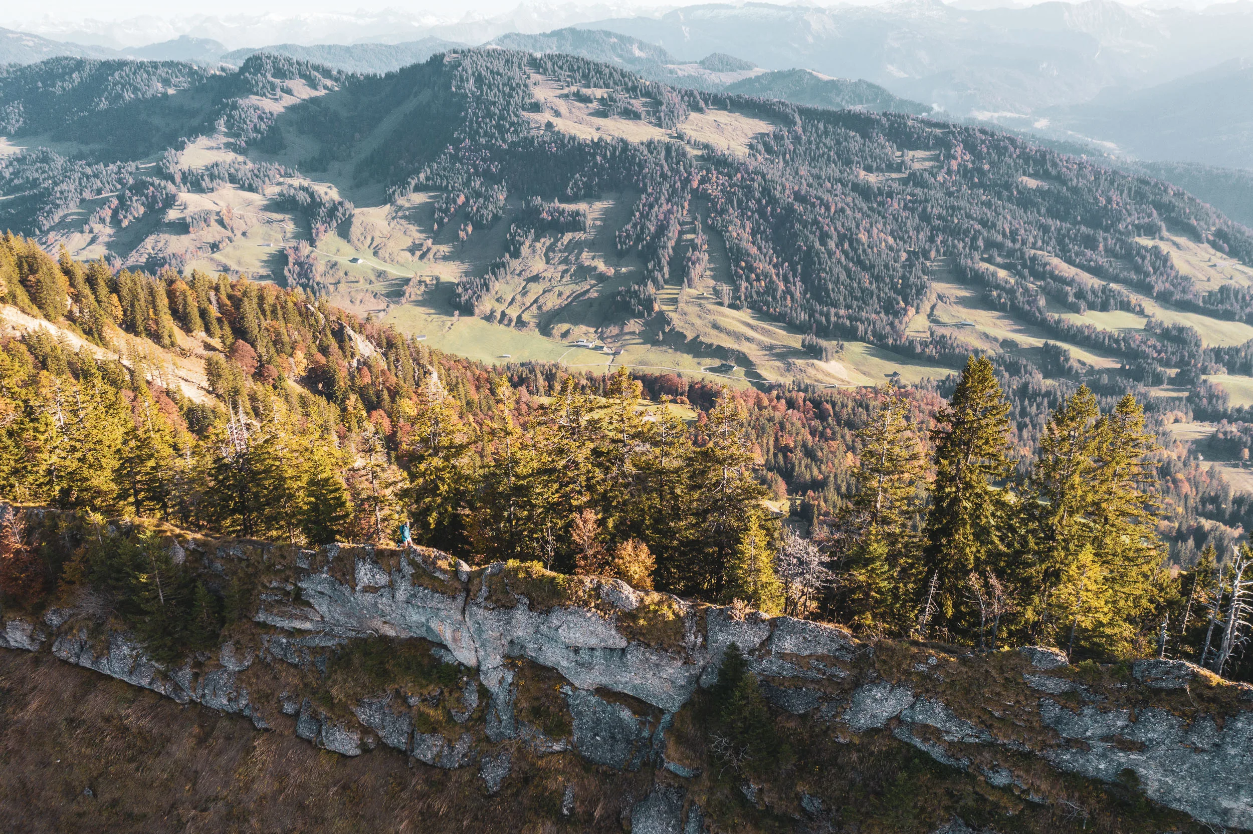 Weite Luftaufnahme der Nagelfluhkette mit felsigen Kämmen, Wald und farbigen Herbsthängen.