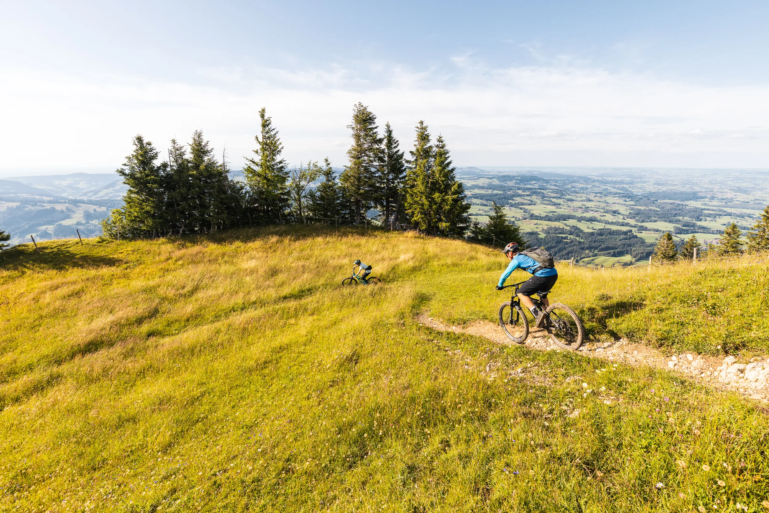 Mountainbiker durchfährt eine Trailkurve auf der Bergwiese mit weitem Blick ins Allgäu