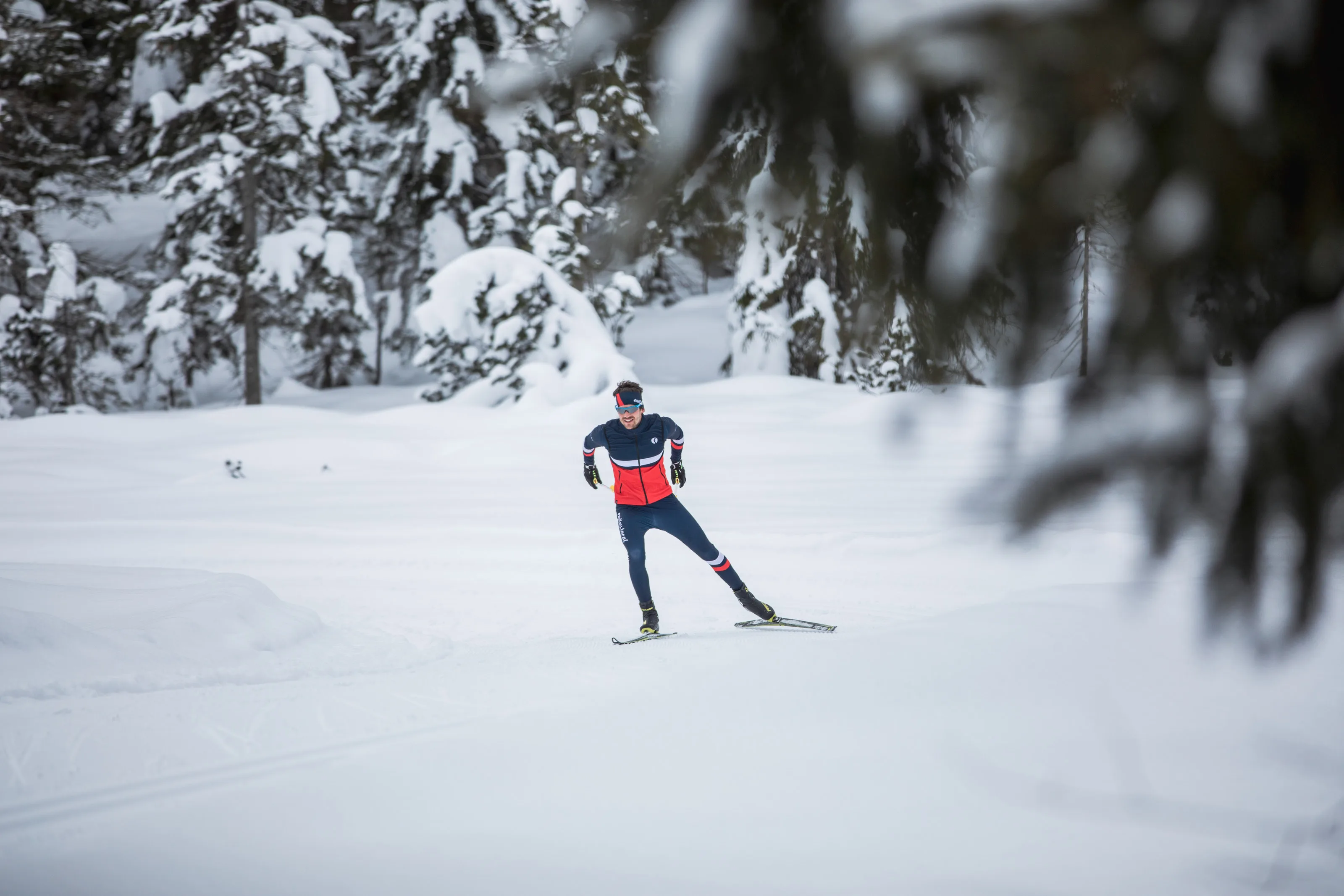 Michael Schnetzer beim Skating-Langlauf, eingerahmt von verschneiten Fichten im Vordergrund.